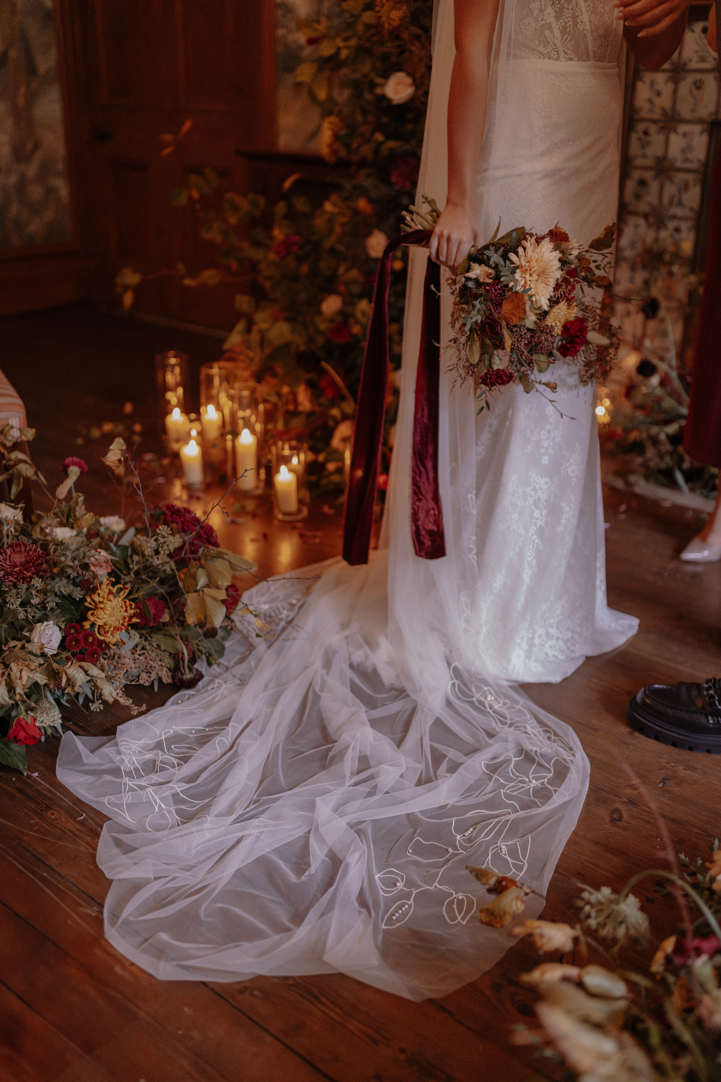A Little Wild, A Little Luxe: Helen Rose Photography's Beautiful Peak District Editorial 18 romantic capture of a bride's veil puddled on the floor amidst Autumn flowers and surrounded by candles. Her hands clutch an elegant Autumn wedding bouquet with silk and velvet ribbons.
