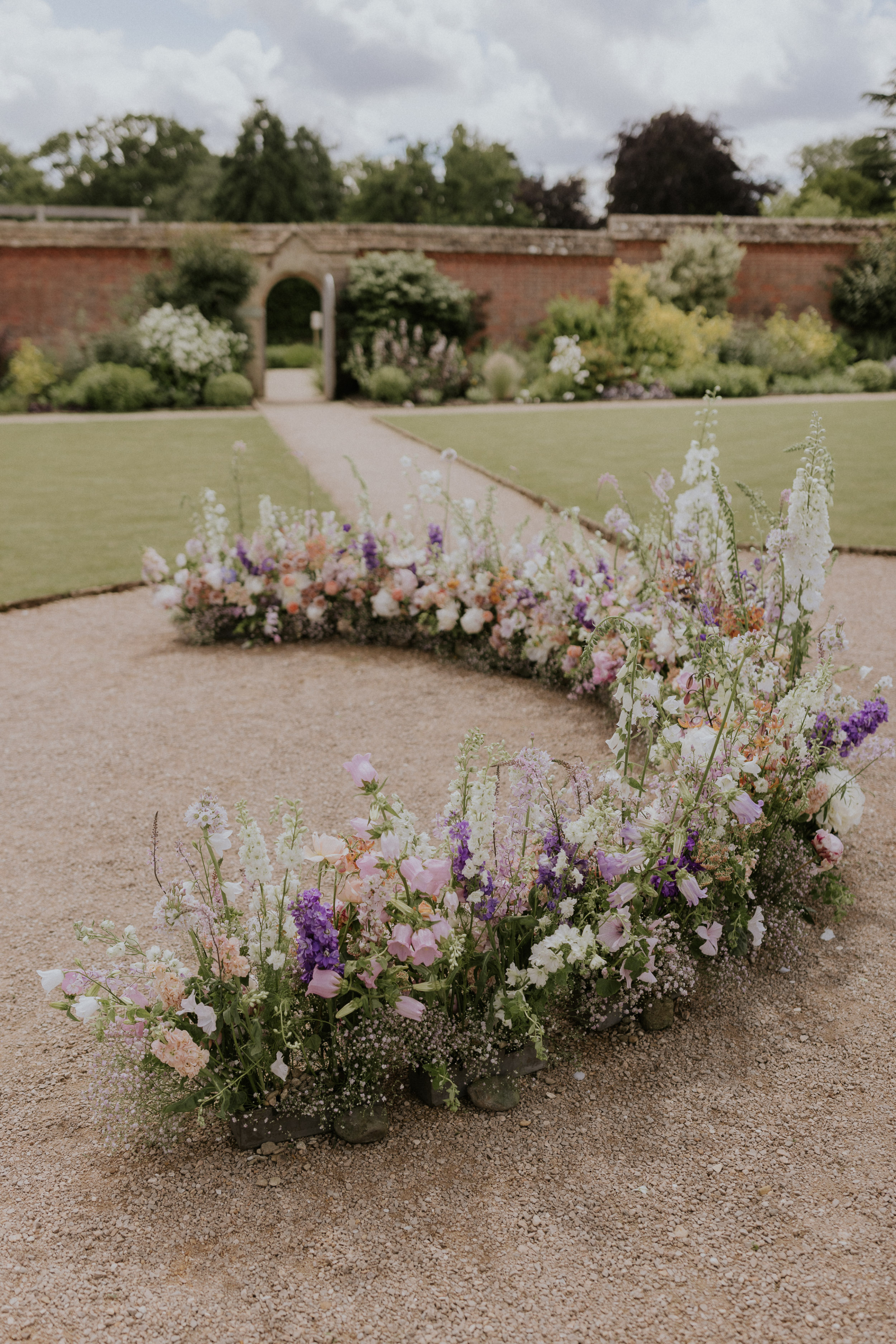 A Romantic Summer Wedding at Kin House in Wiltshire 33 A curved arrangement of wedding flowers for an outdoor wedding ceremony at Kin House in Wiltshire. Maja Tsolo Photography.
