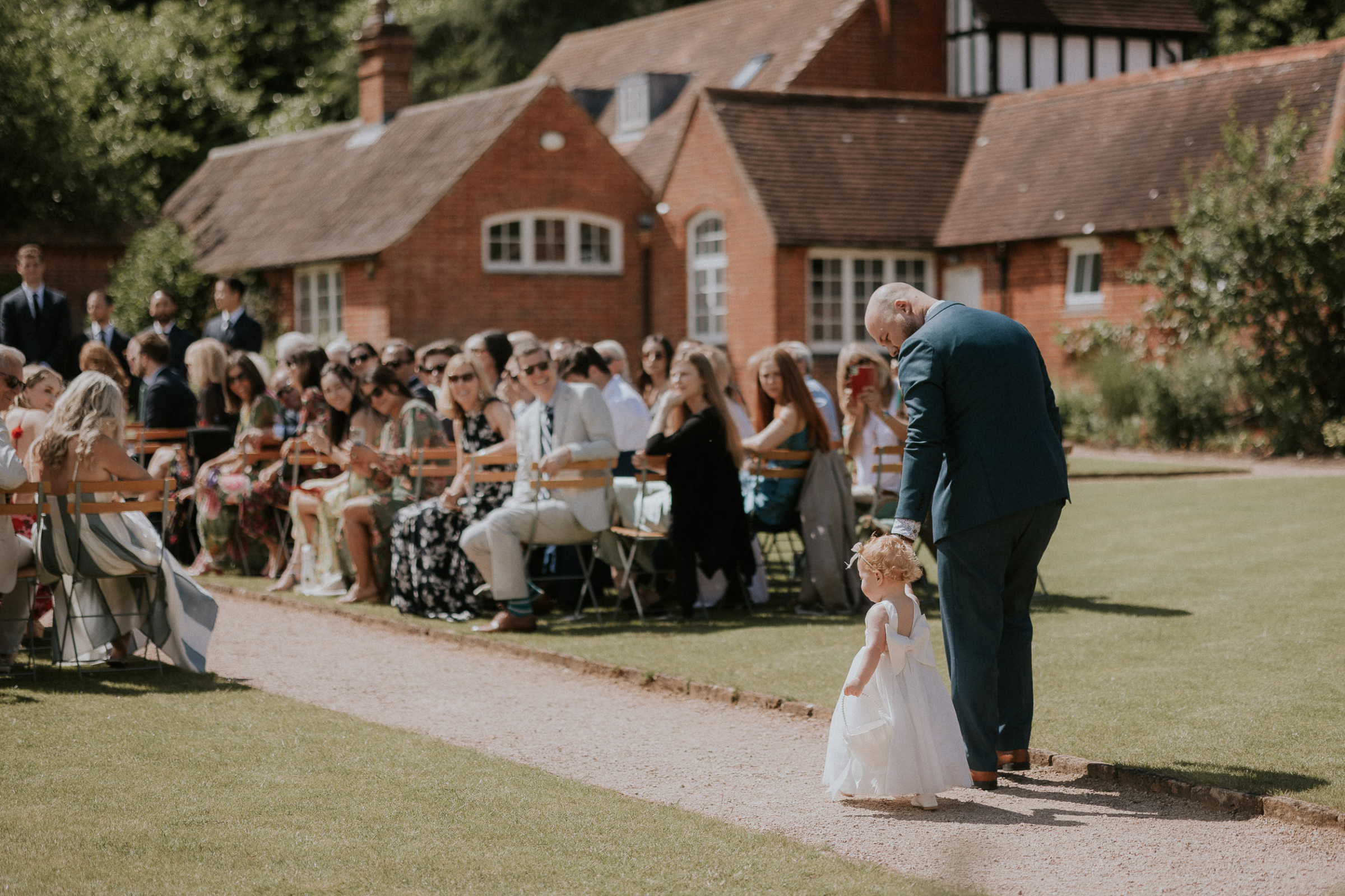 A Romantic Summer Wedding at Kin House in Wiltshire 34 Toddler flower girl walking down the aisle with her father. She wears a cute dress with a large bow at the back from H&M. Maja Tsolo Photography.