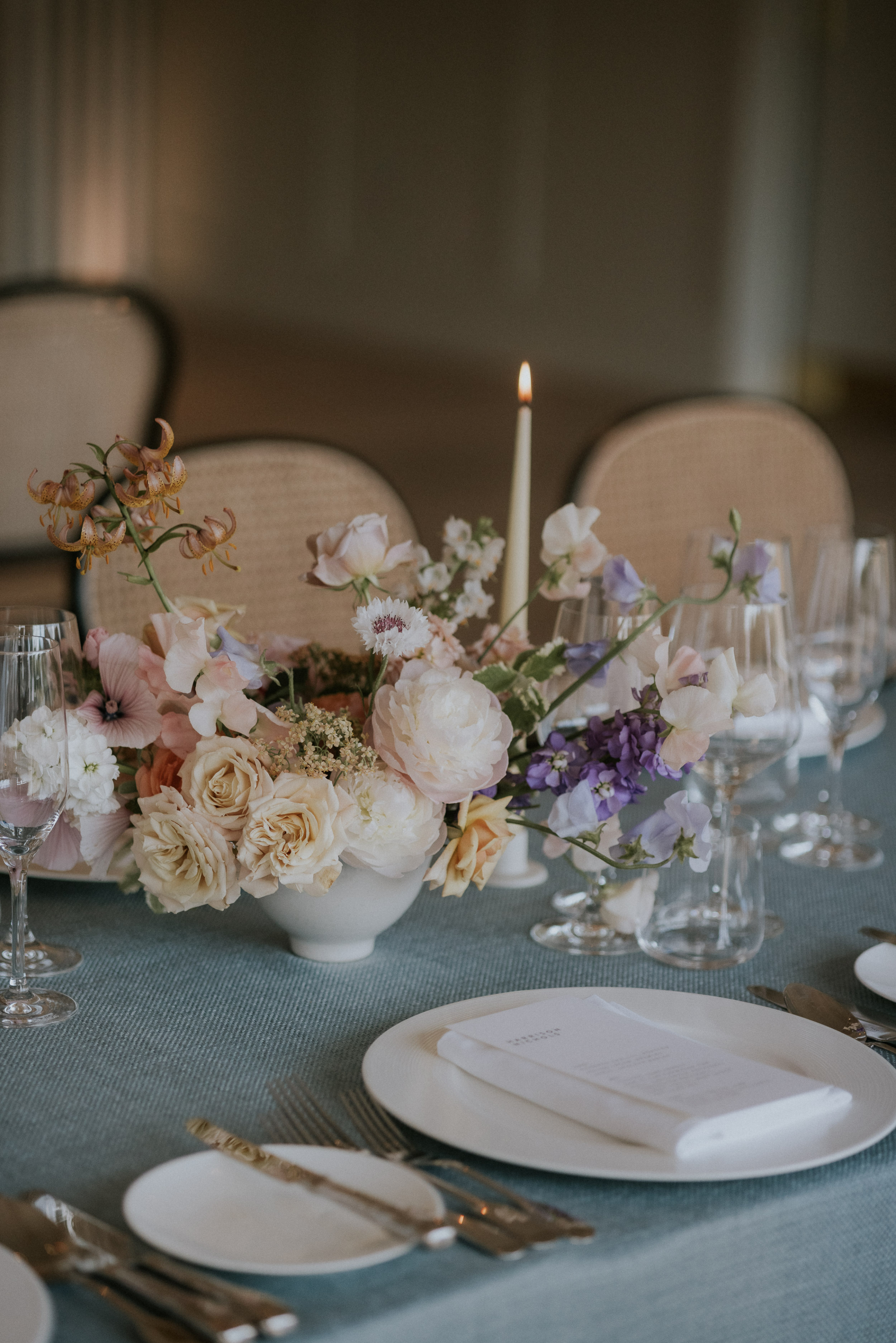 Beautiful low bowl floral displays with pastel flowers, pale taper candles and pale blue linen. Maja Tsolo Photography.