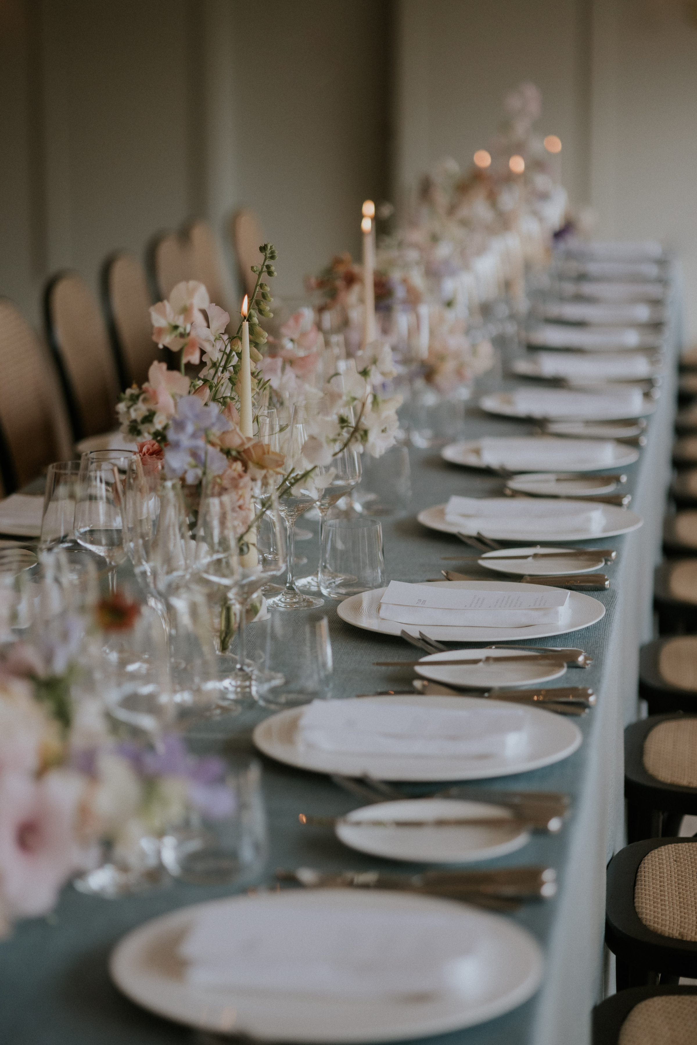 Pastel colour wedding flowers and pale peach taper candles lining the centre of long tables at Kin House wedding venue in Wiltshire. Maja Tsolo Photography.