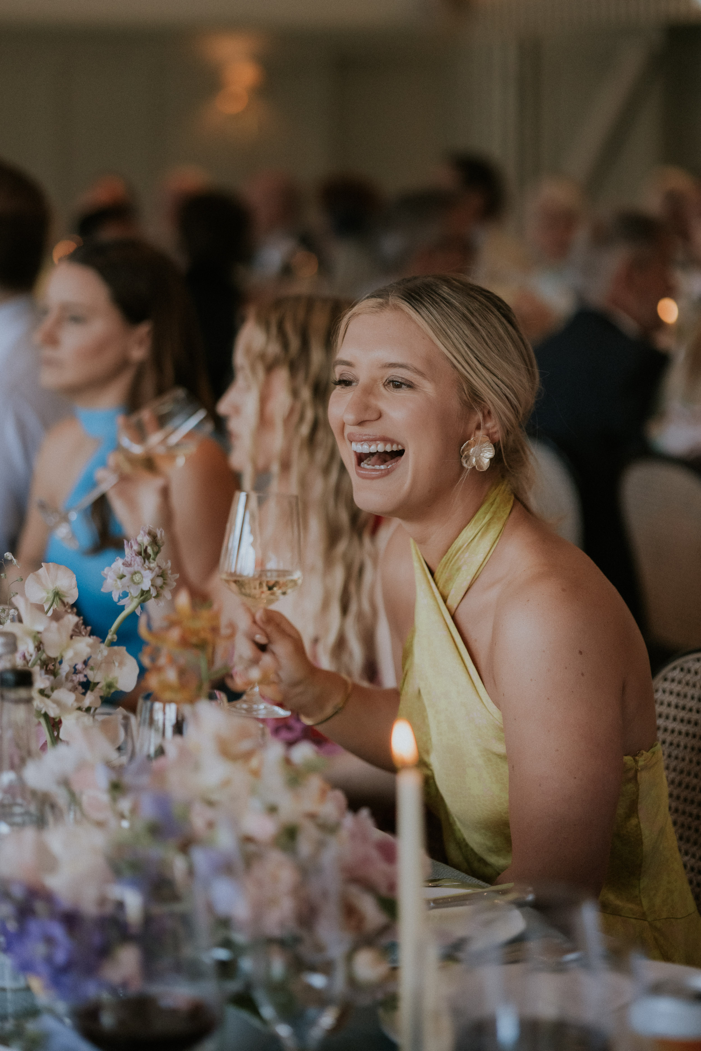 Wedding guest dressed in a yellow dress laughing with happiness at a wedding reception. Maja Tsolo Photography.