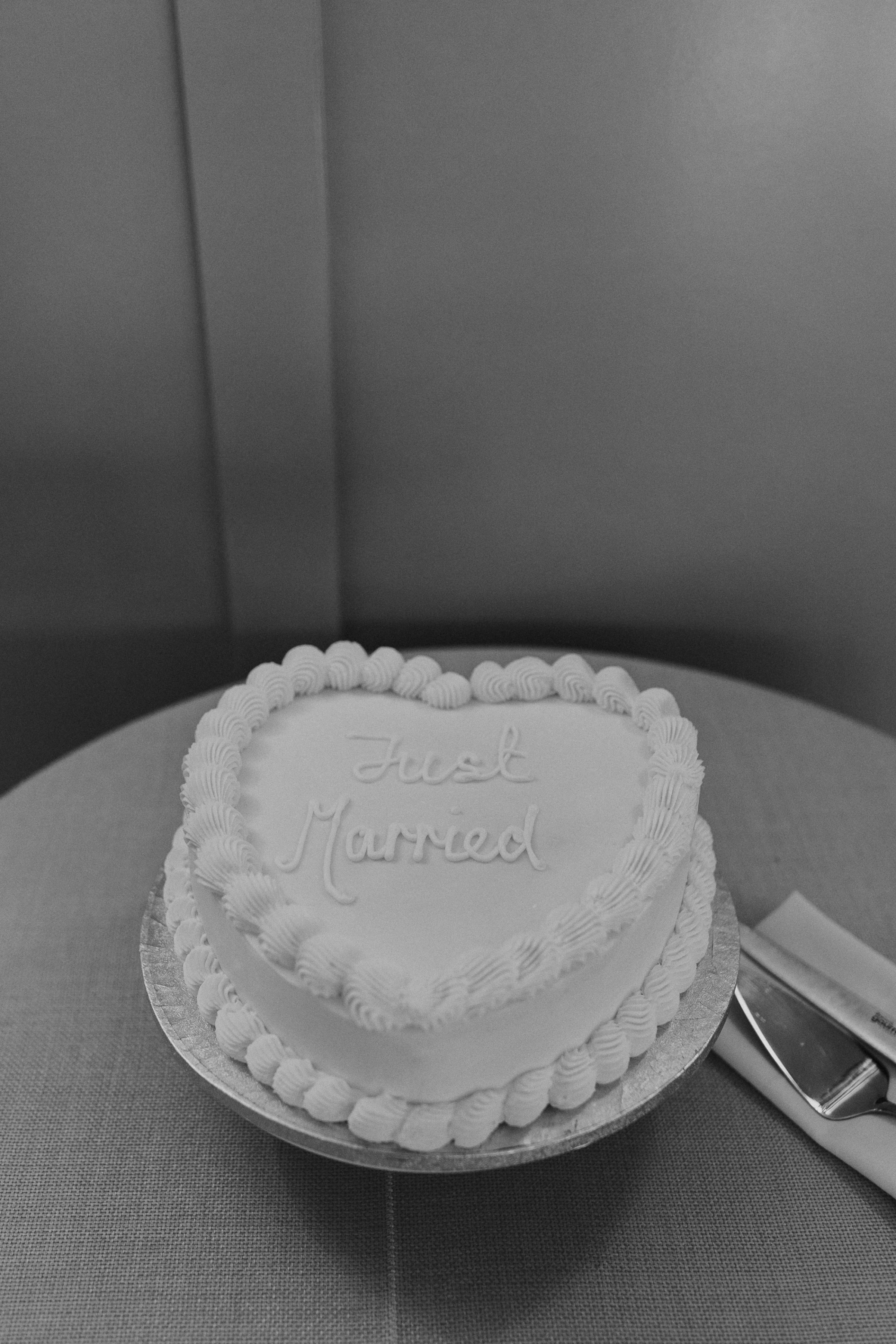 Single tier wedding cake shaped like a heart with frilly icing and the words 'Just married' iced on the top. Maja Tsolo Photography.