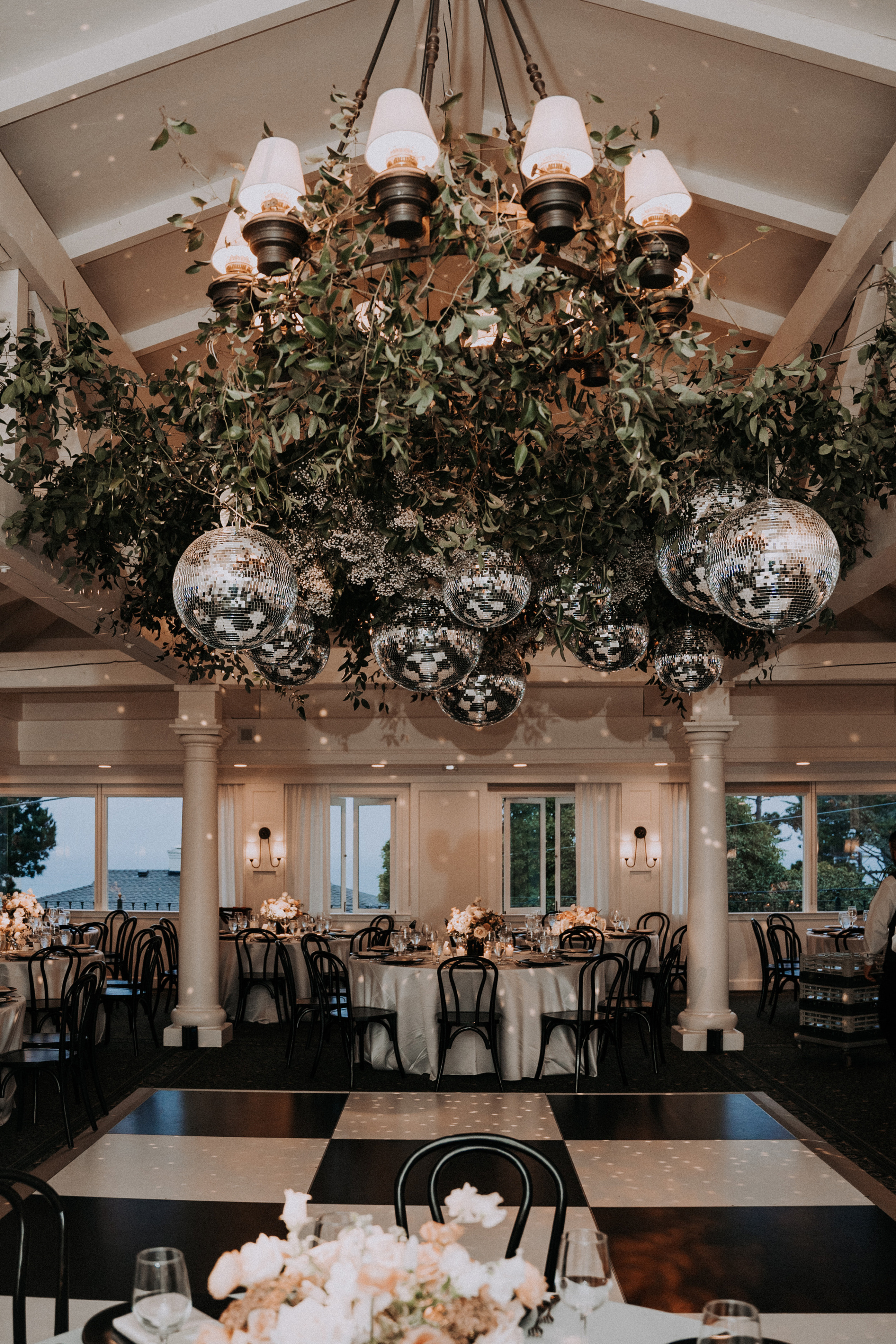 Giant disco balls hanging from a metal chandelier above a chequered dance floor.
