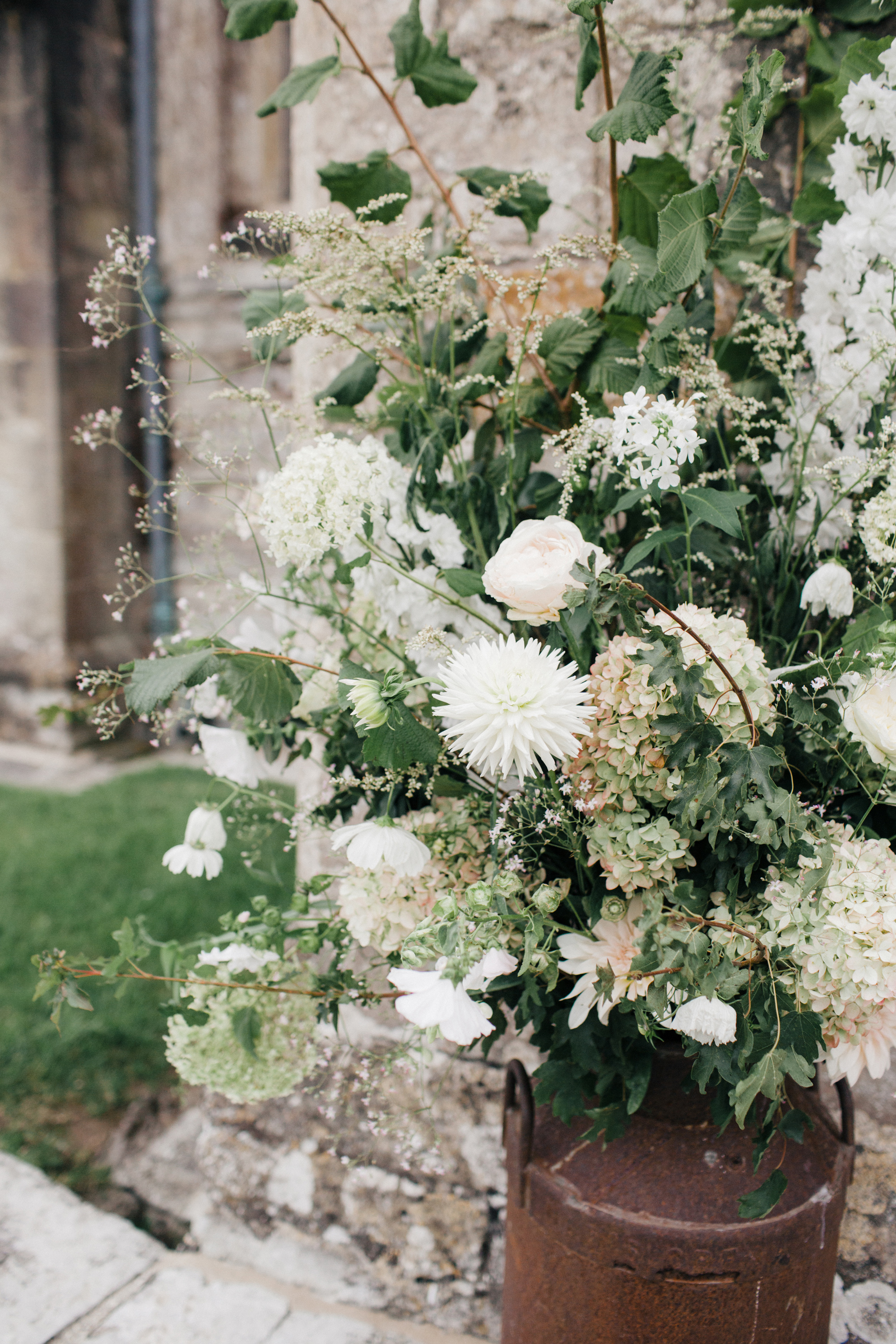 Milk churns outside a church filled with white flowers and foliage.