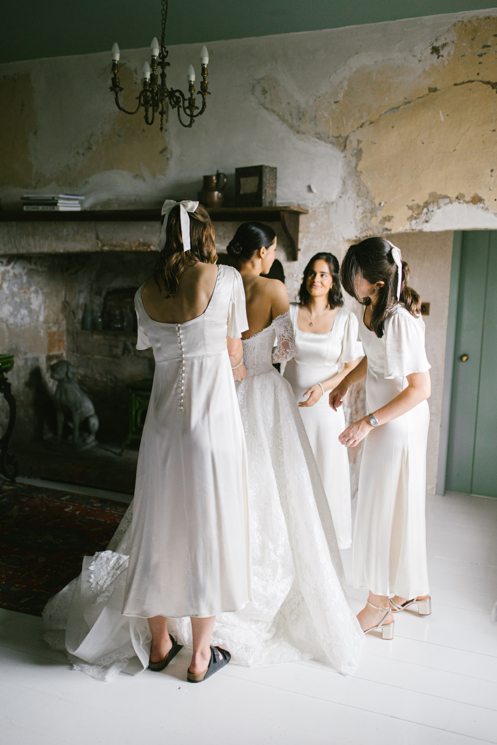 A Josephine Scott Bride & her Romantic Spring Wedding in Somerset 15 Bridesmaids wearing white Nobodys Child dresses and helping the bride into her Josephine Scott wedding dress.
