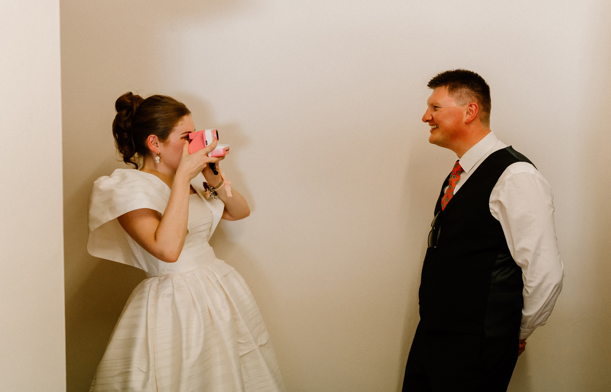 Hannah in Jesus Peiro for her Intimate Brunton House Wedding in Northumberland 49 Bride taking a polaroid photograph of her groom using a pink polaroid camera. She wears a puff sleeve Jesus Peiro wedding dress.
