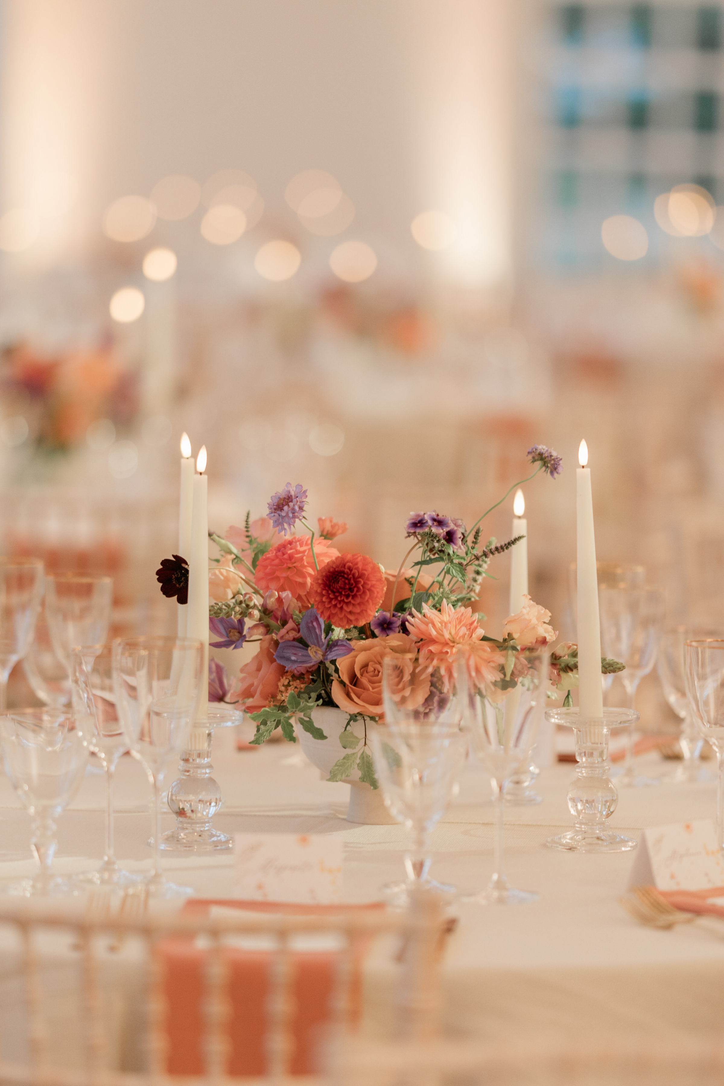 Elegant wedding table setting at Kew Gardens featuring peach napkins, gold cutlery, pale taper candles and colourful floral table centrepieces.