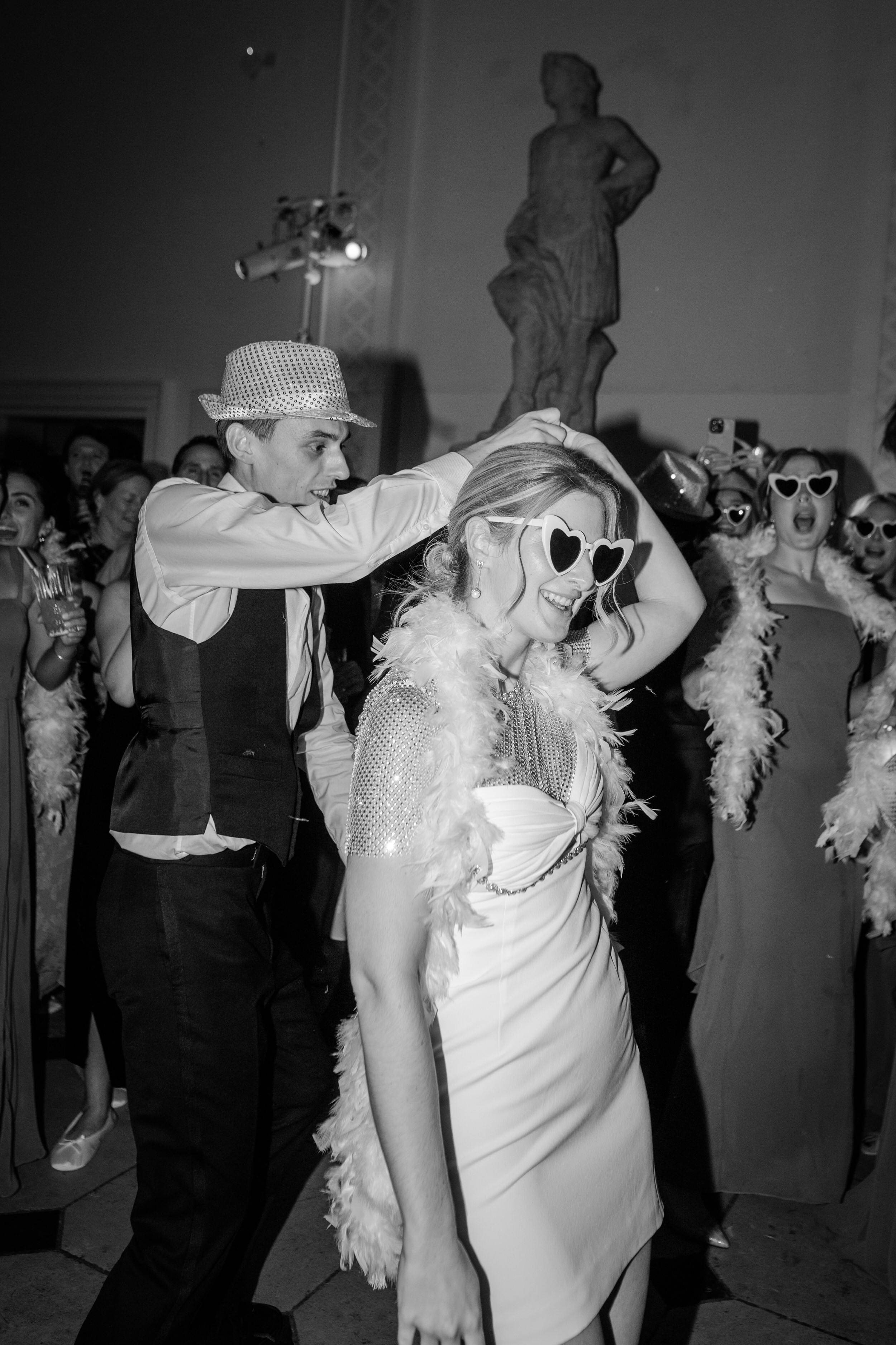 A Dreamy Kew Gardens Glasshouse Wedding Planned by Rachel Dalton 45 Groom in a hat and bride in a feather boah and heart sunglasses.