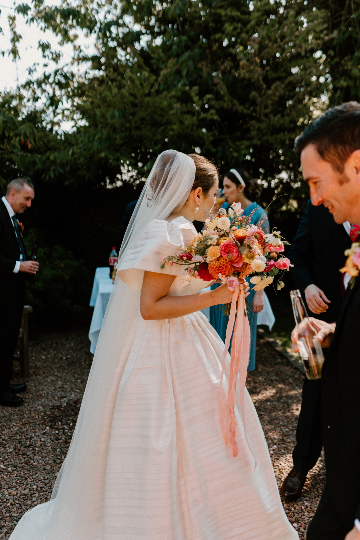 Hannah in Jesus Peiro for her Intimate Brunton House Wedding in Northumberland 34 Bride in a puff sleeve Jesus Peiro wedding dress holding a colourful late summer early Autumn wedding bouquet with Dahlia and roses, and peach silk ribbons. She wears a veil over her bun and pearl drop earrings.
