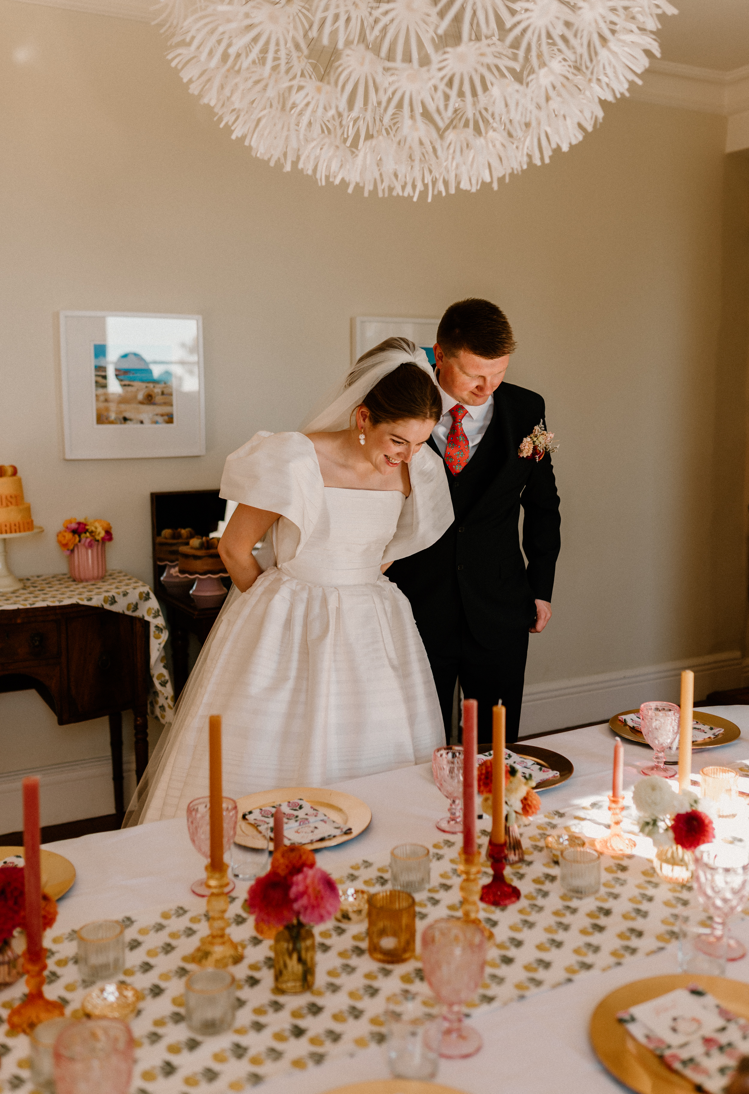 Hannah in Jesus Peiro for her Intimate Brunton House Wedding in Northumberland 40 Bride and groom observing their wedding table settings with glee. She wears a puff sleeve Jesus Peiro wedding dress and veil over her high bun.