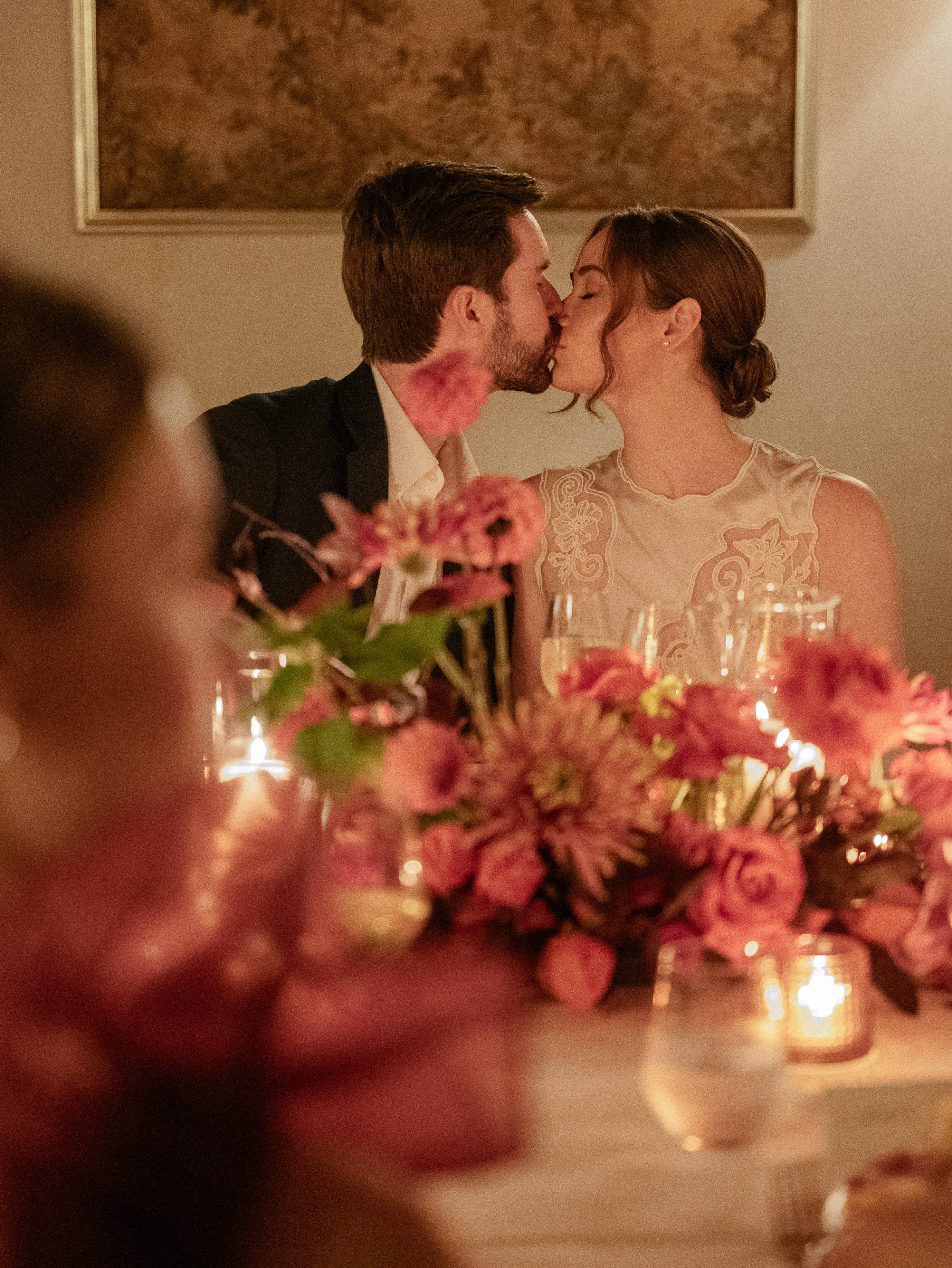 Bride and groom kissing between the candles and flowers during a romantic evening rehearsal dinner at Relais La Corte Dei Papi wedding venue in Cortana, Italy.