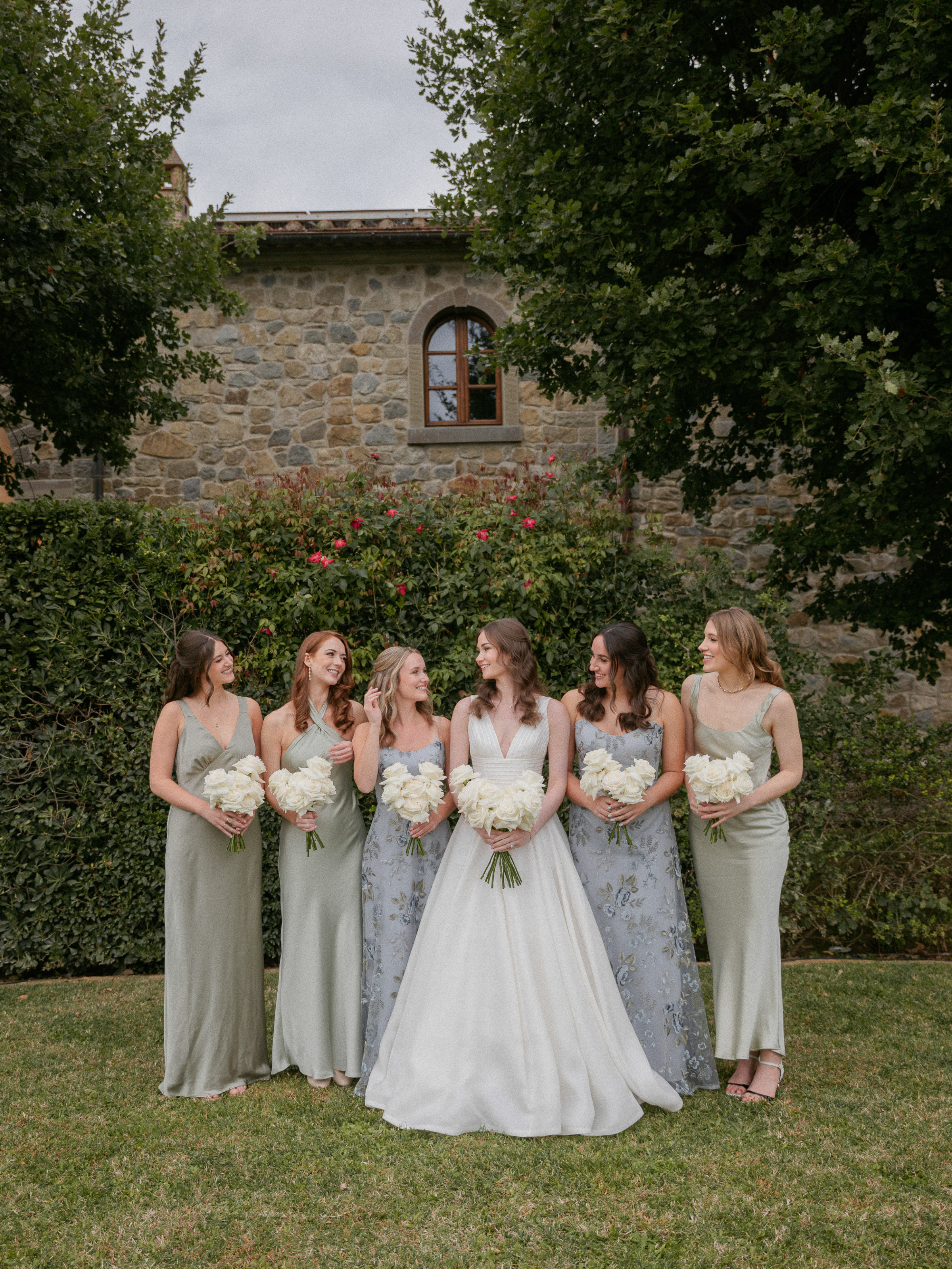 An Elegant Destination Wedding in Cortona, Italy, with a Peter Langner Gown 24 Bride wearing a Peter Langner wedding dress and carrying a bouquet of white flexed roses. Her bridesmaids wear pale sage green and blue floral dress by Jenny Yoo.