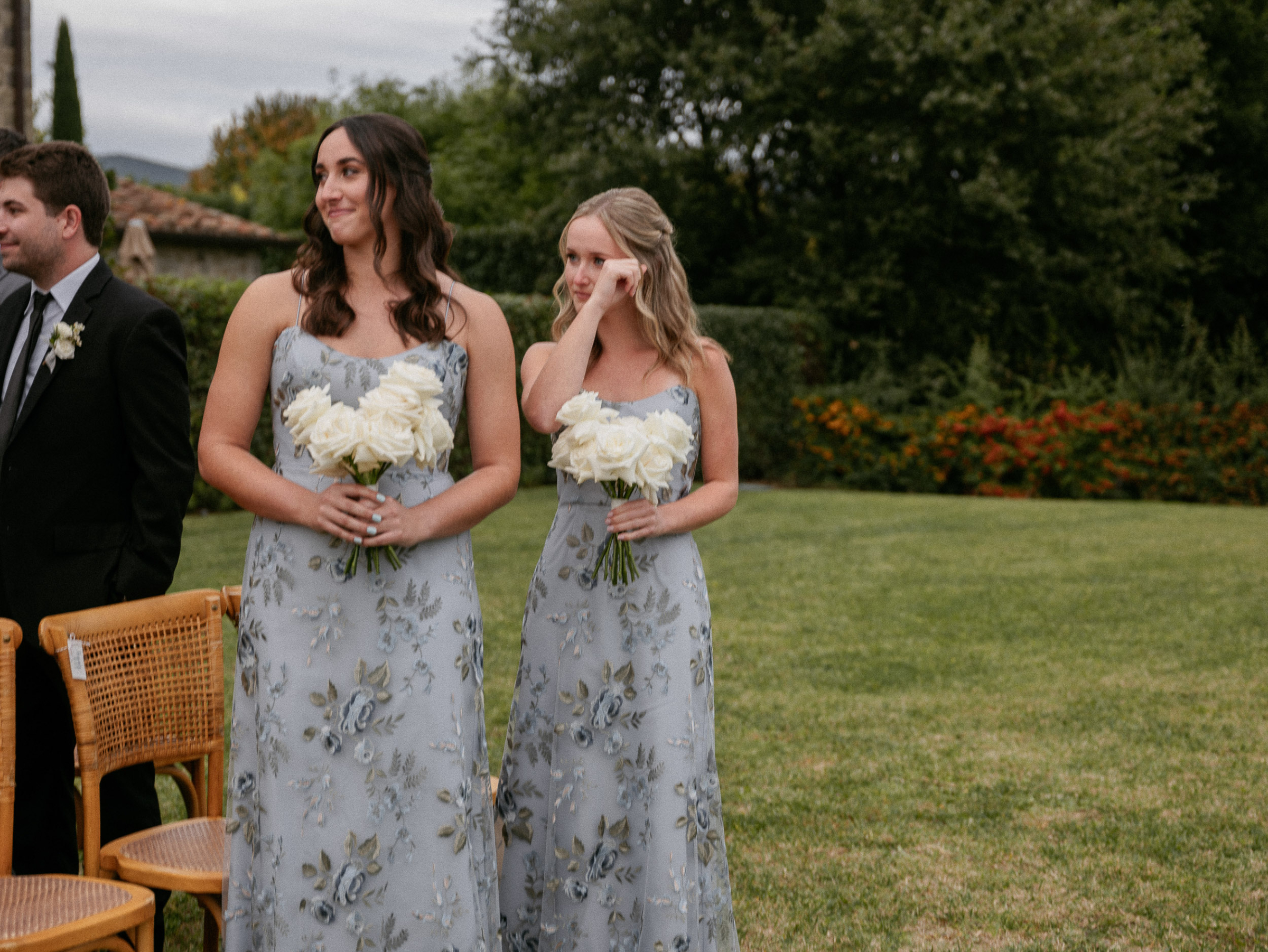 Bridesmaids in blue floral dresses wiping happy tears during an outdoor Italian wedding ceremony at  Relais La Corte Dei Papi in Cortona in Italy.