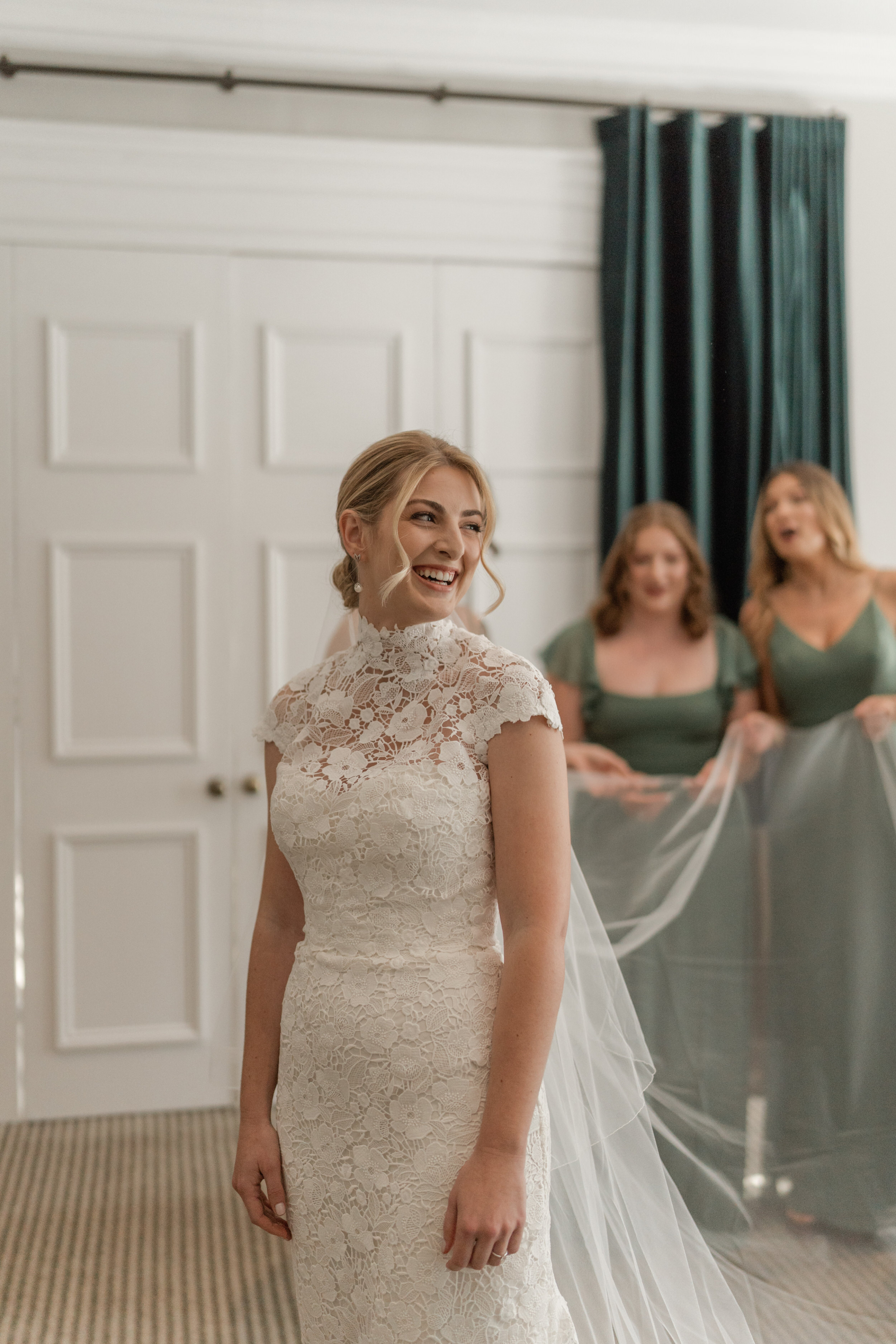 A Dreamy Kew Gardens Glasshouse Wedding Planned by Rachel Dalton 21 Brides in sage green dresses holding the veil of the bride, who wears a lace halterneck wedding dress by Mark Ingram.