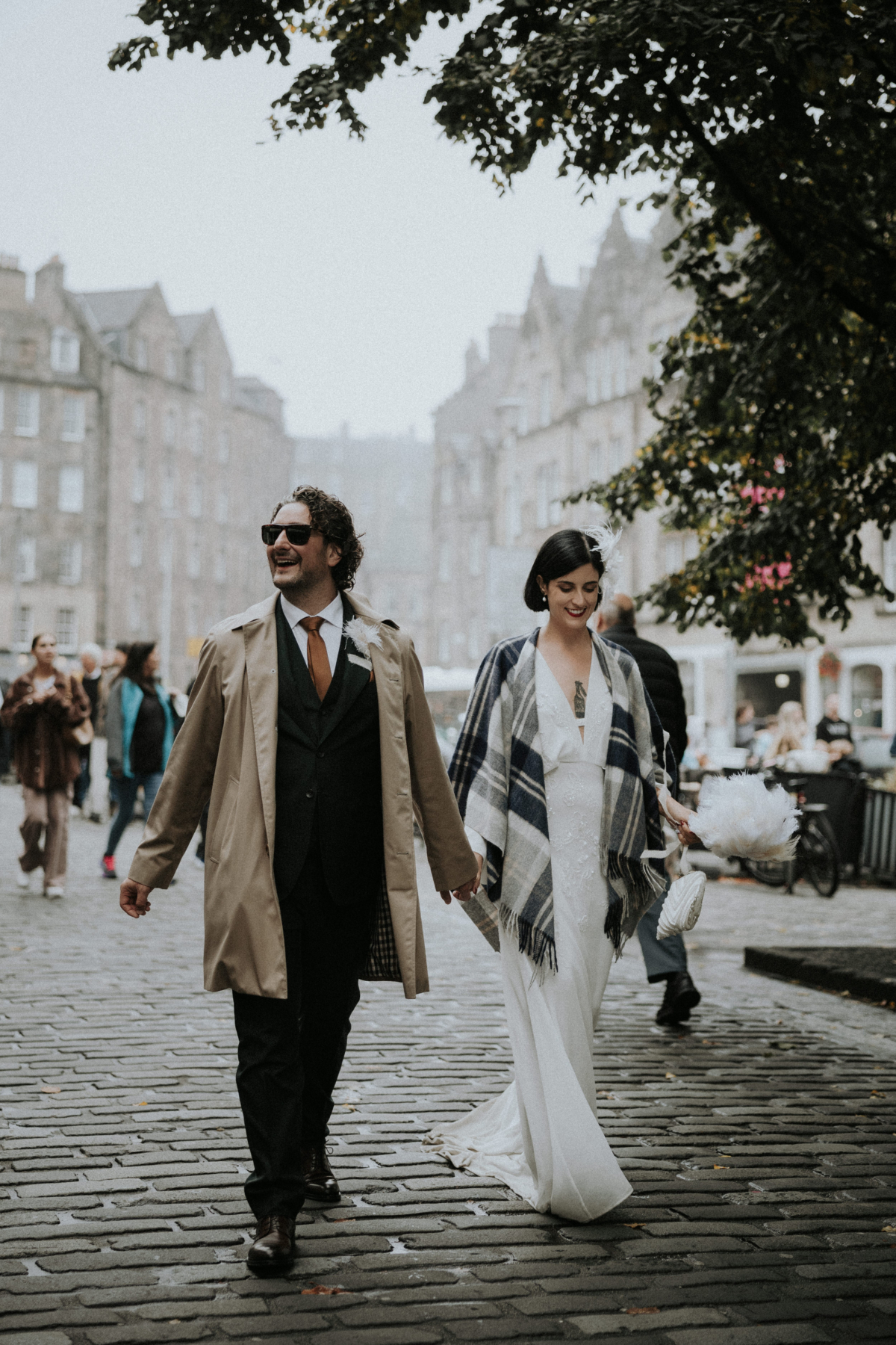 A Chic, Modern & Intimate Edinburgh City Wedding with an ASOS Dress 7 Modern bride and groom walking through the cobbled streets of Edinburgh. The bride wears a tartan throw over her wedding dress. Bernadeta Kupiec Photography.