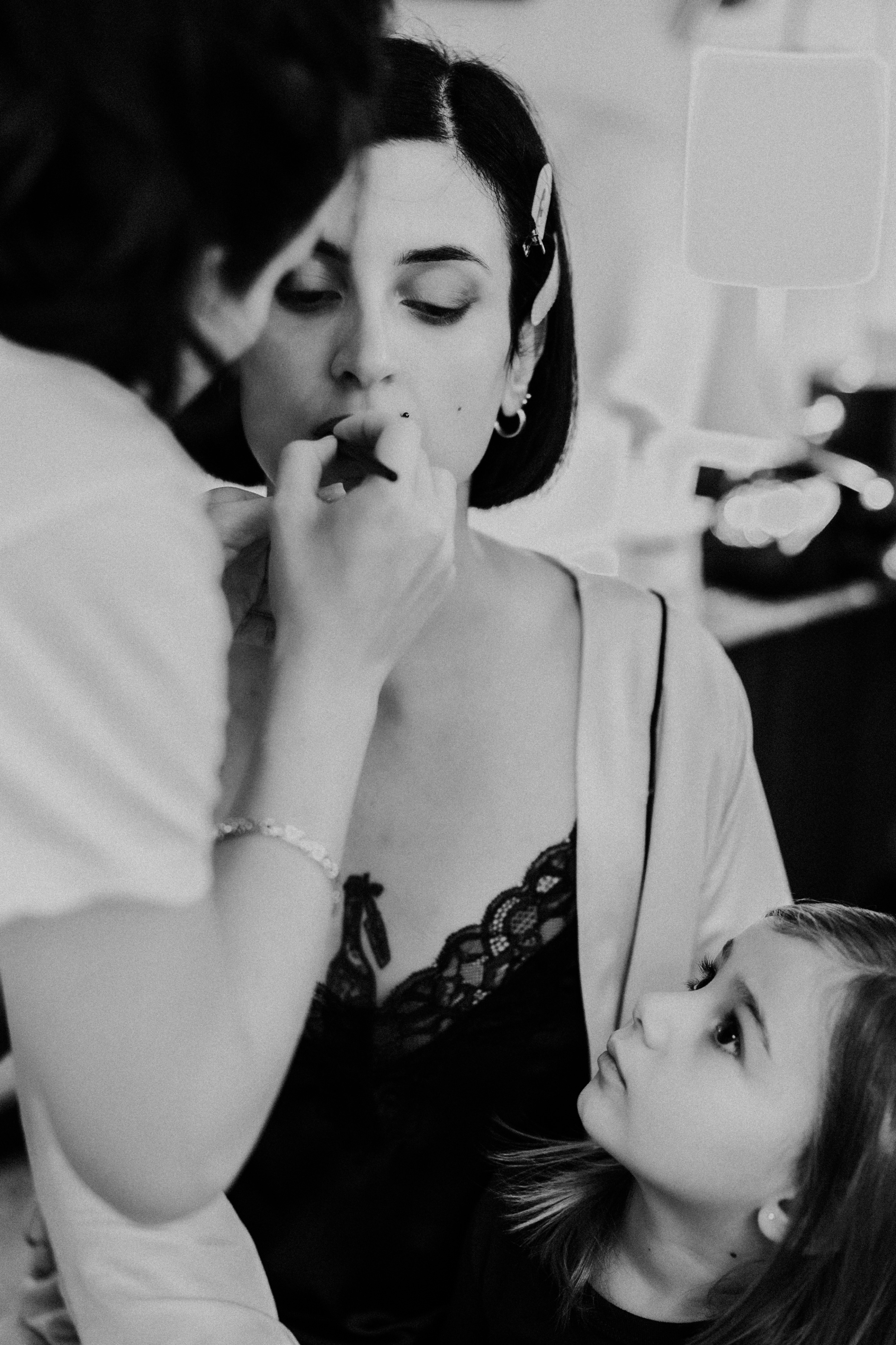 Black and white photography of bride in a black lace slip having her makeup professionally applied. Bernadeta Kupiec Photography.