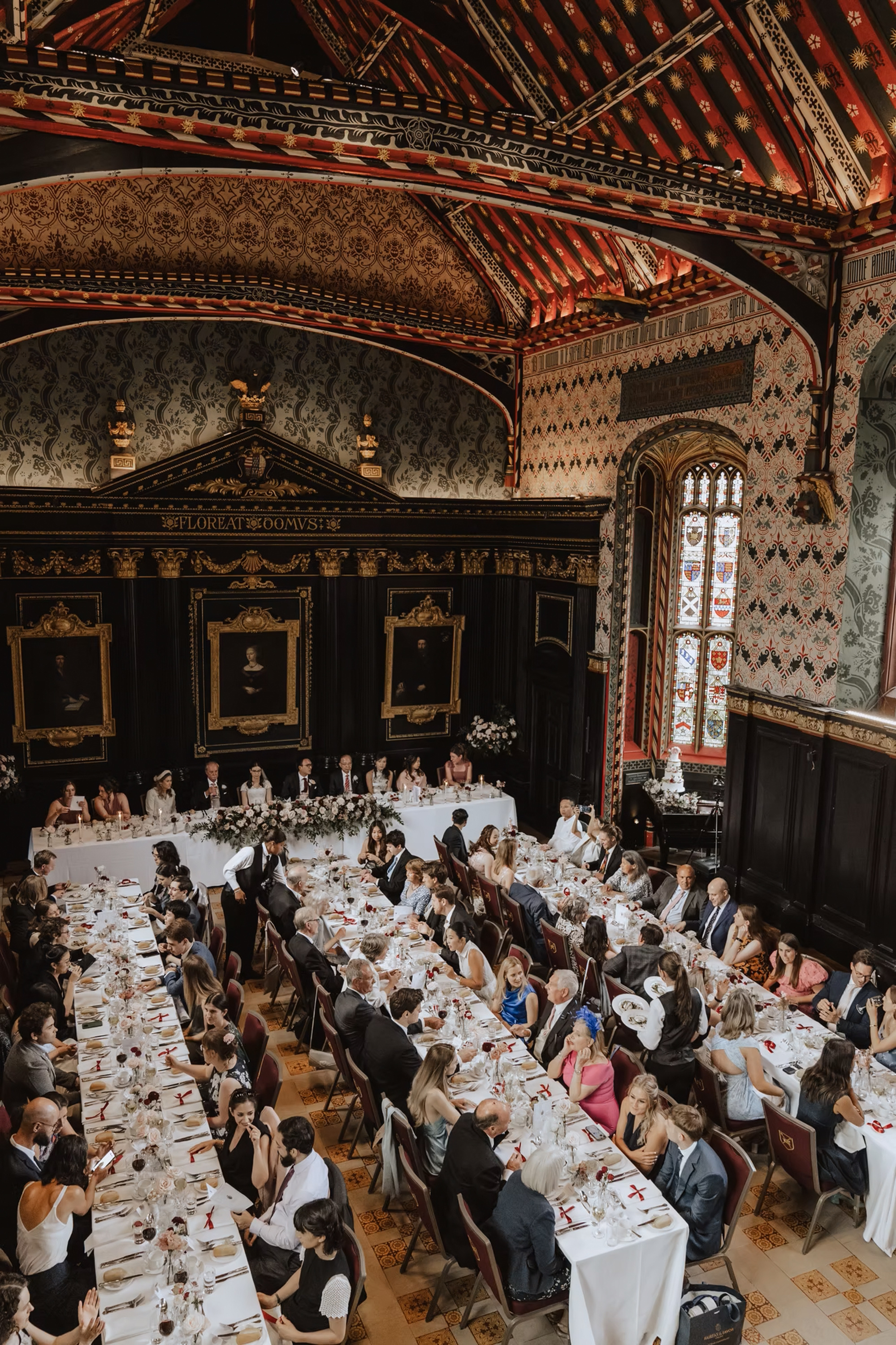 Tall elegant wedding reception venue lined with long reception tables where people are seated eating. Vivienne May Weddings & Events - UK wedding planner. 