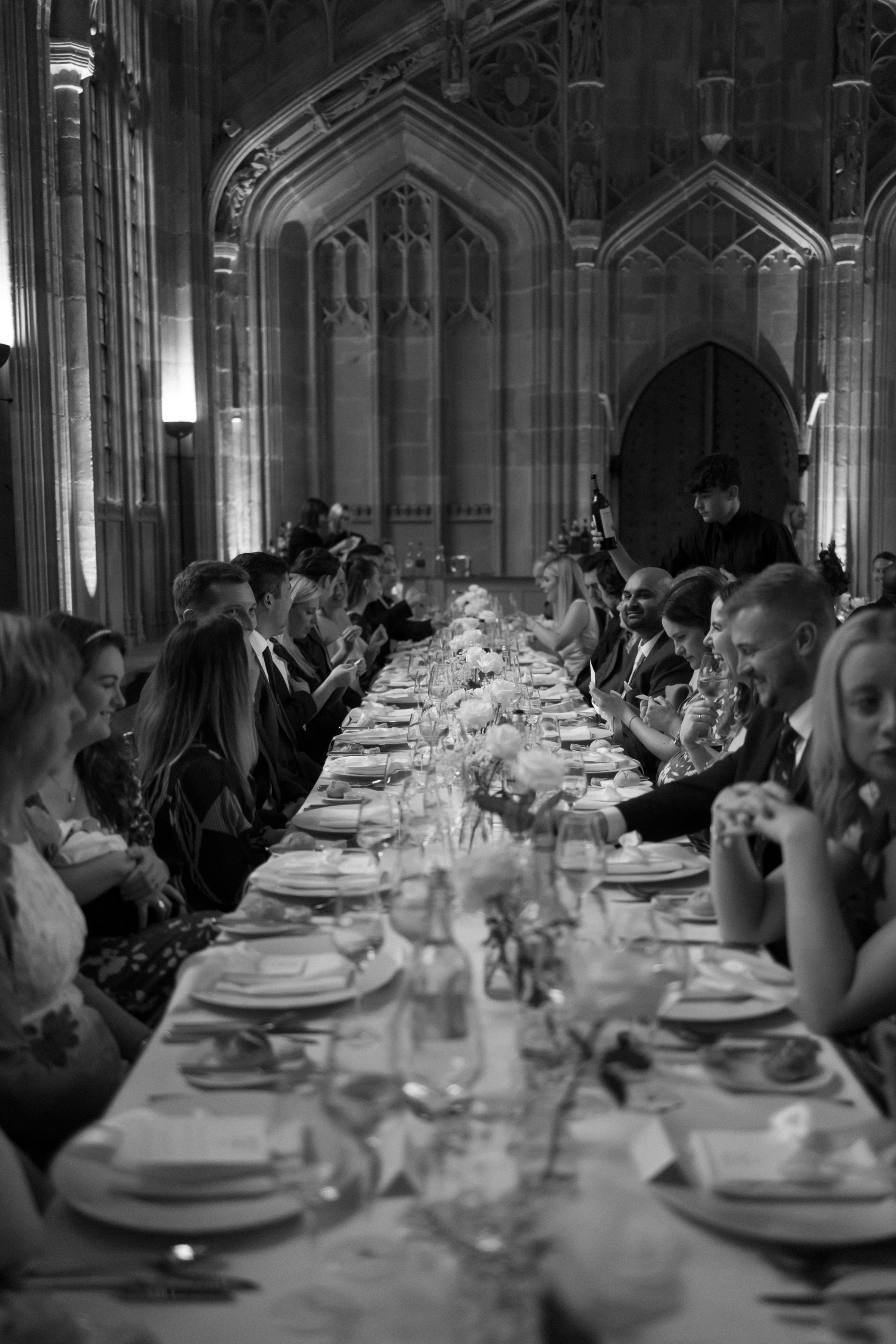 Black-and-white image of wedding guests dining under vaulted gothic arches at the Bodleian Library, creating an elegant and timeless reception scene.