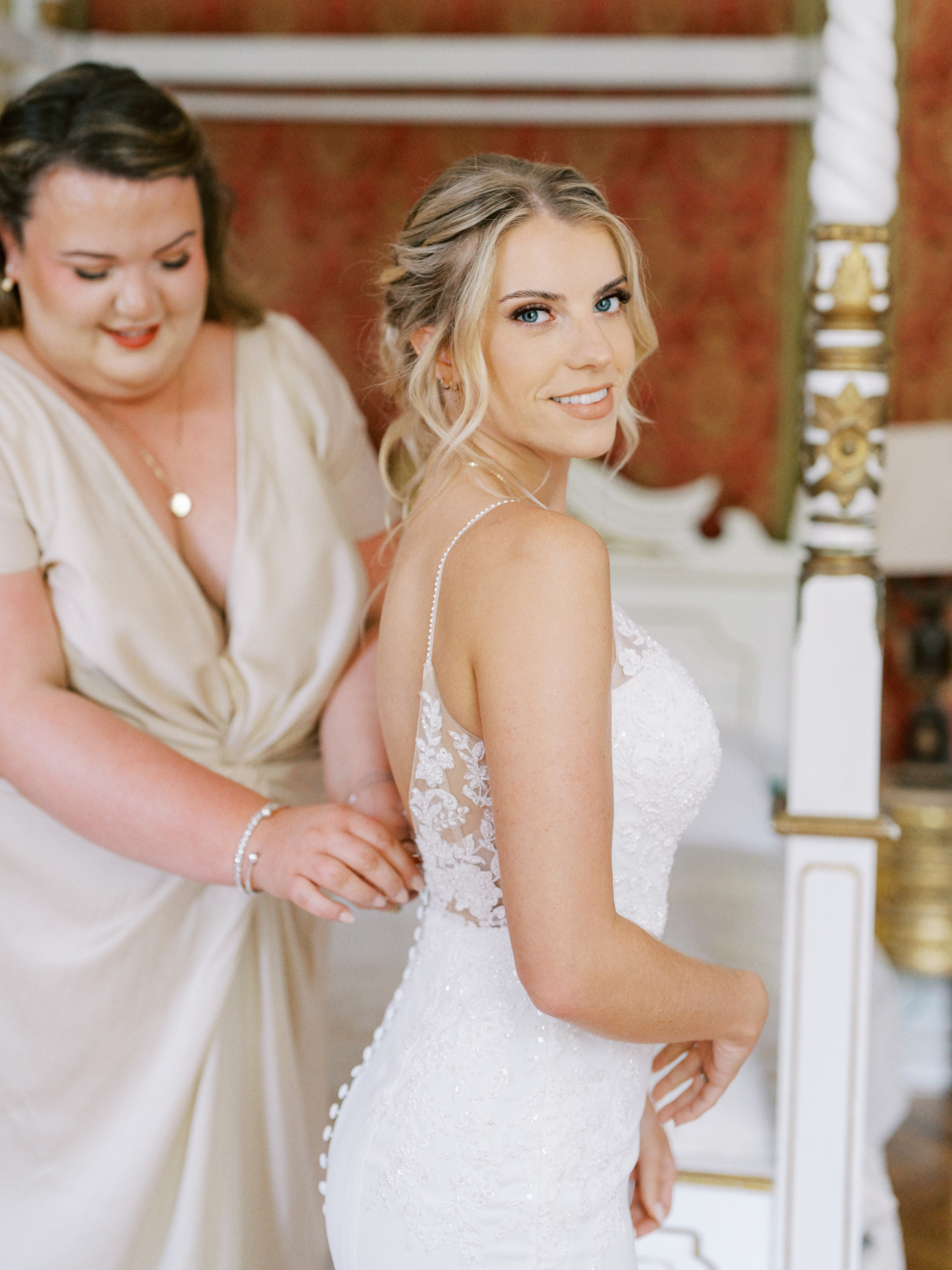 An Elegant Modern Wedding at Chateau de Robernier 59 Bride being fitted into her lace dress with pearl straps.
