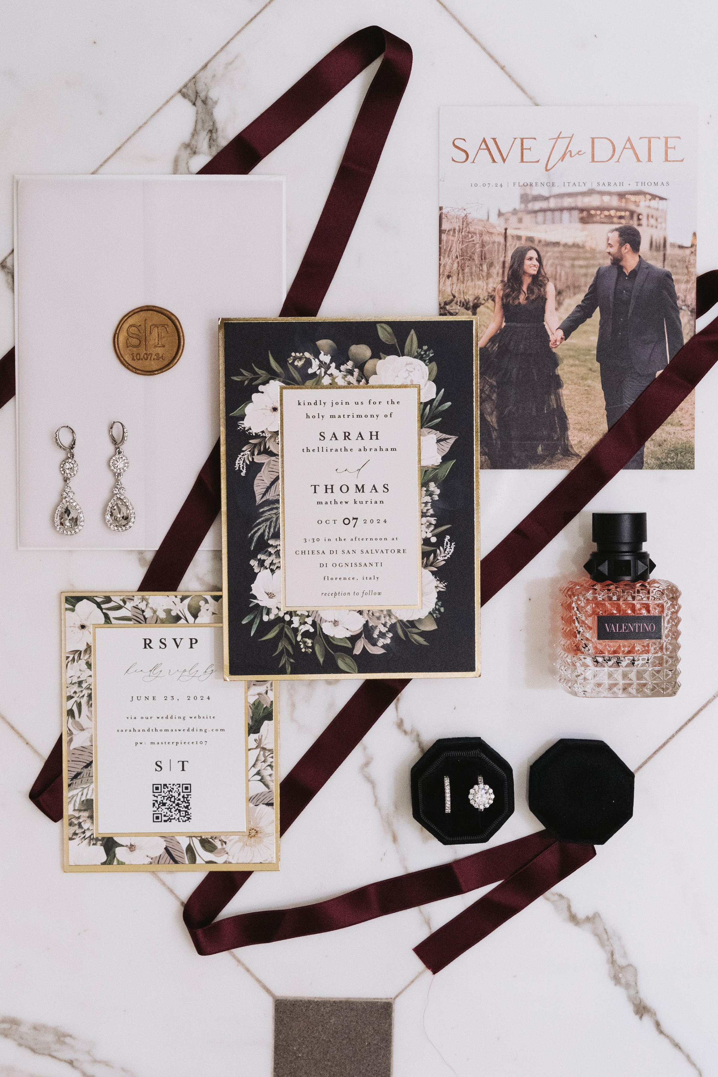 Black floral wedding stationery flat lay with Valentino perfume and dark silk ribbon.