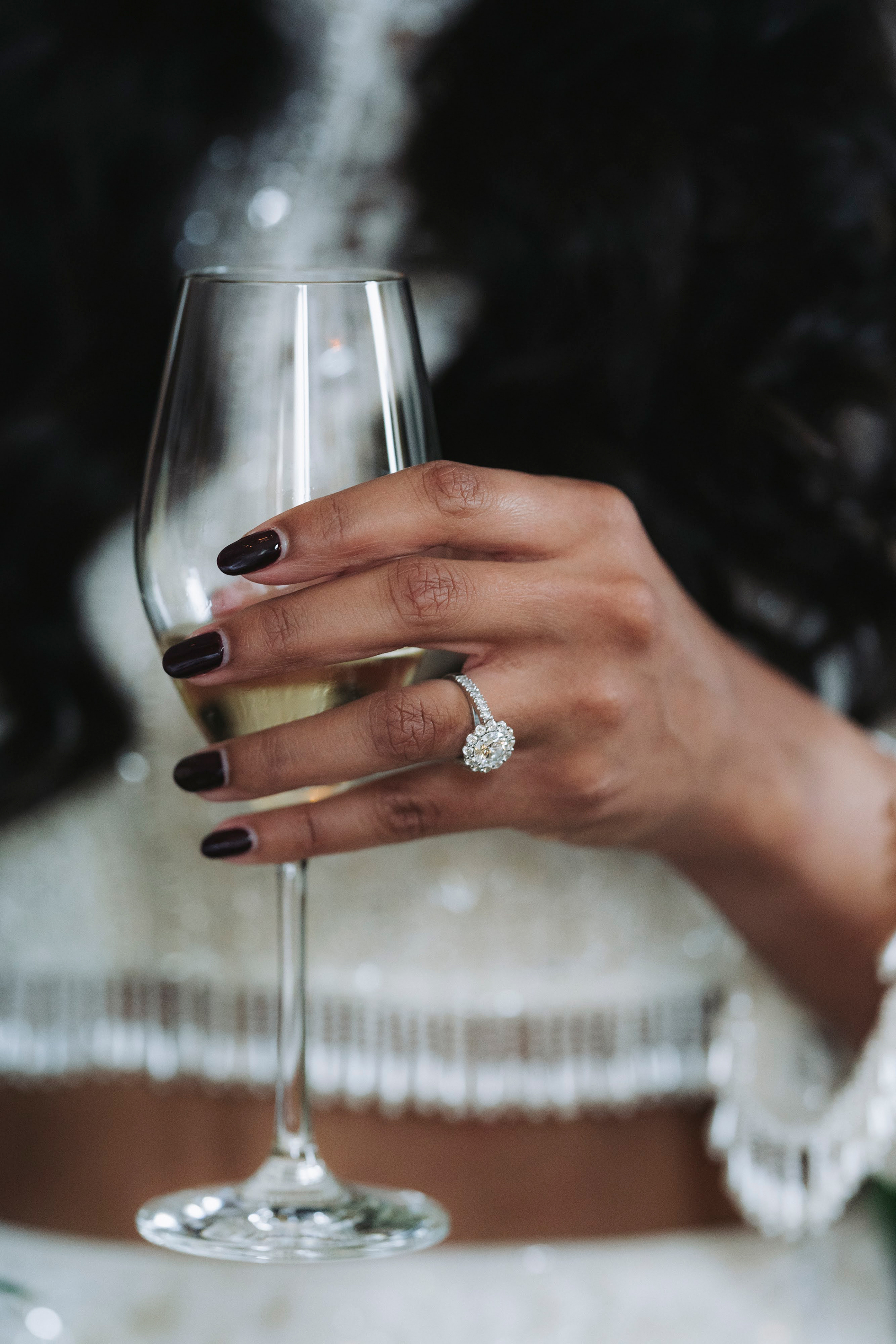 Close up shot of Indian bride with a black manicutre and a large diamond engagement ring.She holds s glass of champagne.