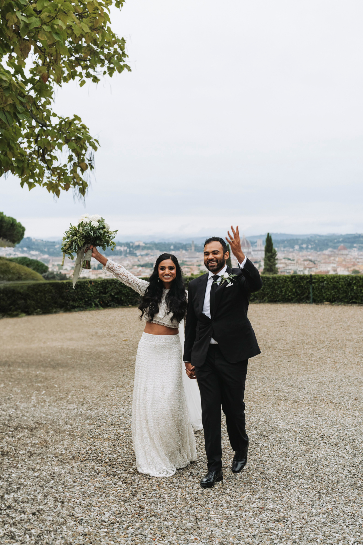 An Elegant Fusion of Indian Tradition and Italian Beauty 82 Modern Indian bride and groom at their Italian wedding. The bride raises her large white and green wedding bouquet in the air with jubiliant joy.