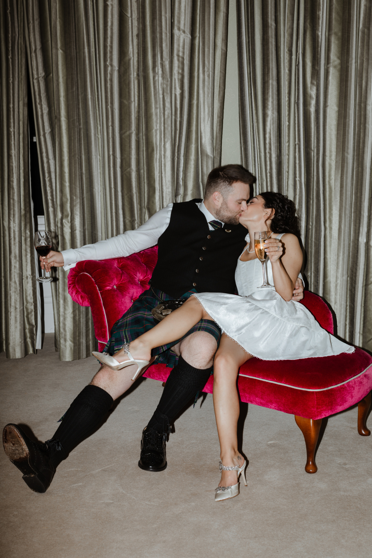 Savannah Miller Elegance for a Joyful Autumn Wedding at Drumtochty Castle 89 Bride and groom laid back on a pink velvet chaise long kissing one another.