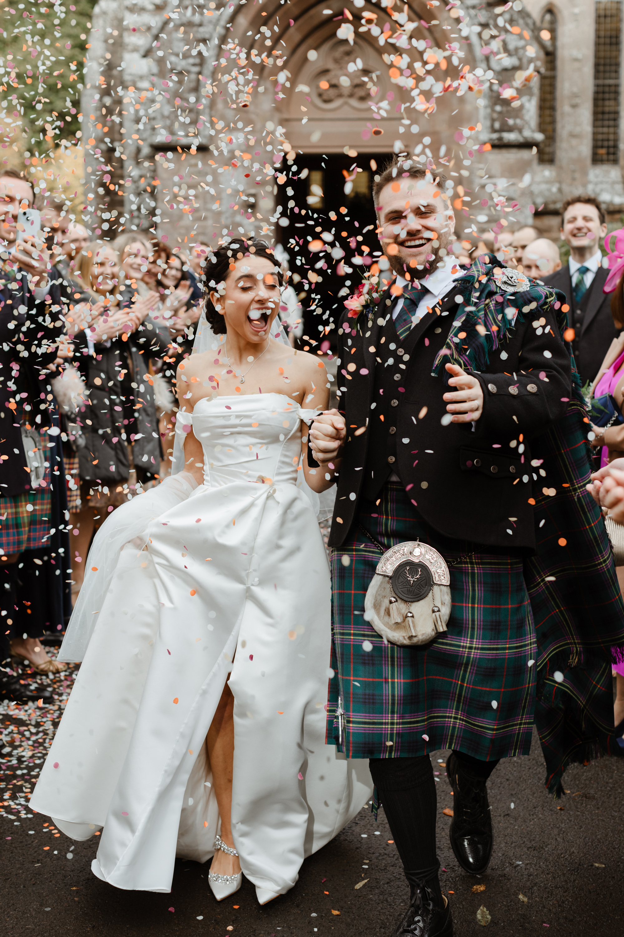 Savannah Miller Elegance for a Joyful Autumn Wedding at Drumtochty Castle 73 Bride and groom exiting the church in a cloud of colourful confetti. The bride wears a Savannah Miller dress.