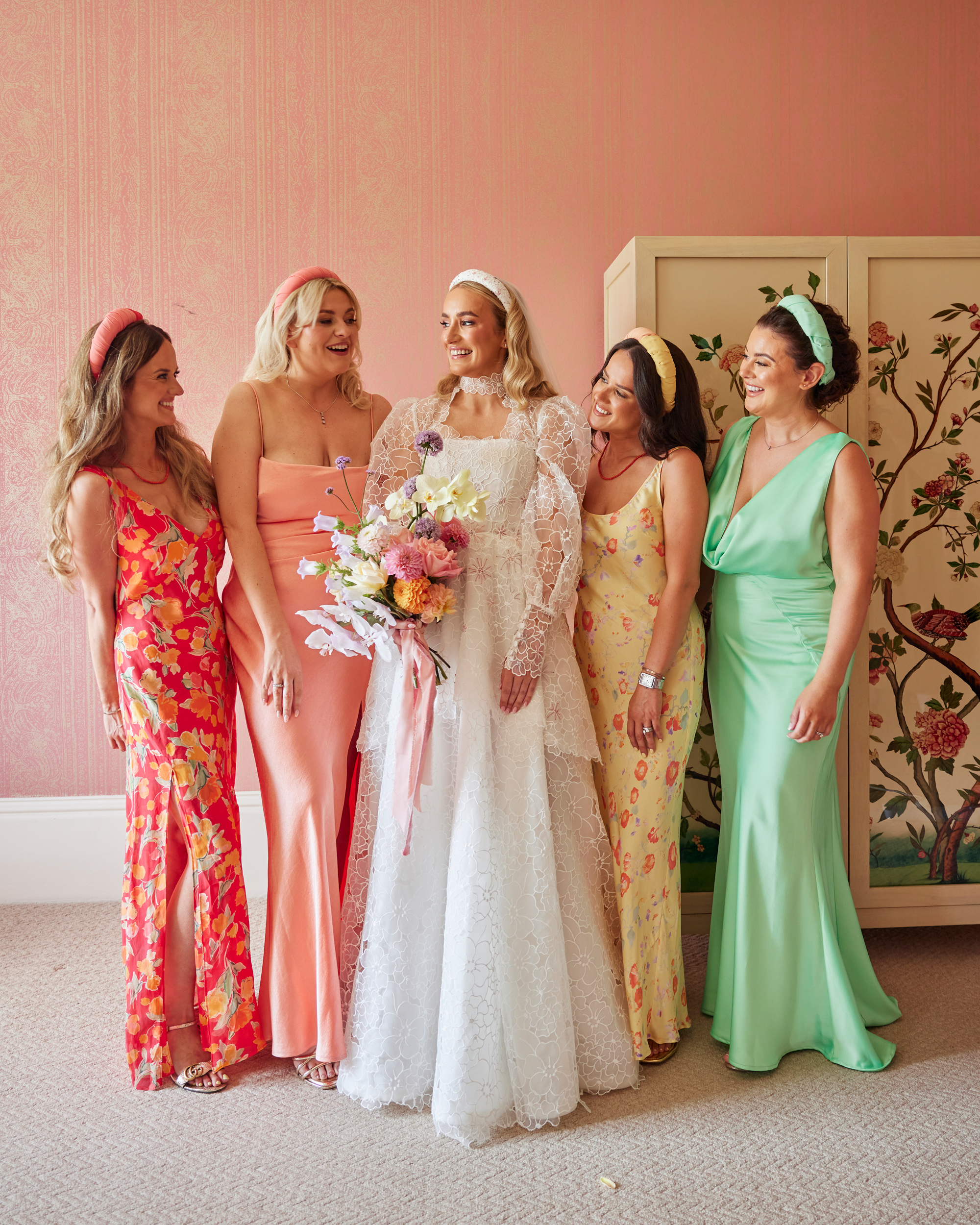 Alex in Emma Beaumont for her Ibiza & Disco Inspired Wedding at Wilderness Reserve 39 Bride in a peplum wedding dress by Emma Beaumont and carrying a pastel wedding bouquet. She is surrounded by her bridesmaids wearing pastel colour dresses and headbands.