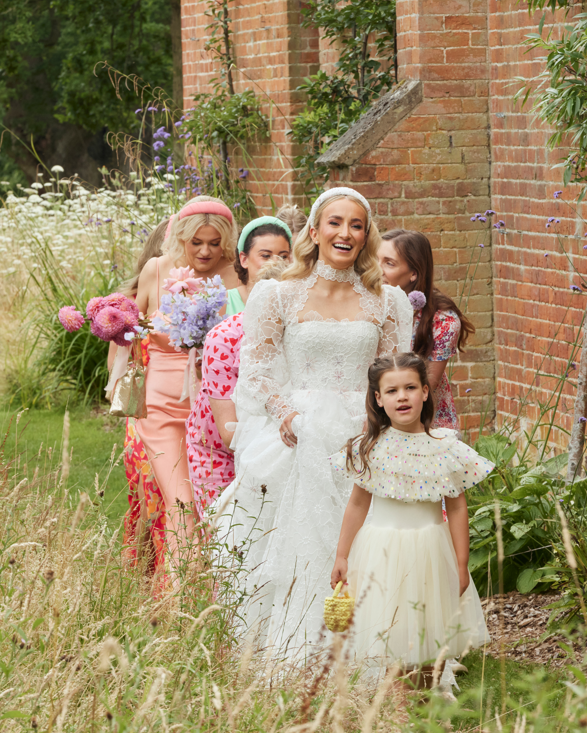 Alex in Emma Beaumont for her Ibiza & Disco Inspired Wedding at Wilderness Reserve 40 Emma Beaumont bride wearing a puff sleeve wedding dress as she walks to the church with her bridesmaids in pastel dresses and flower girls in colourful polkadot tulle.