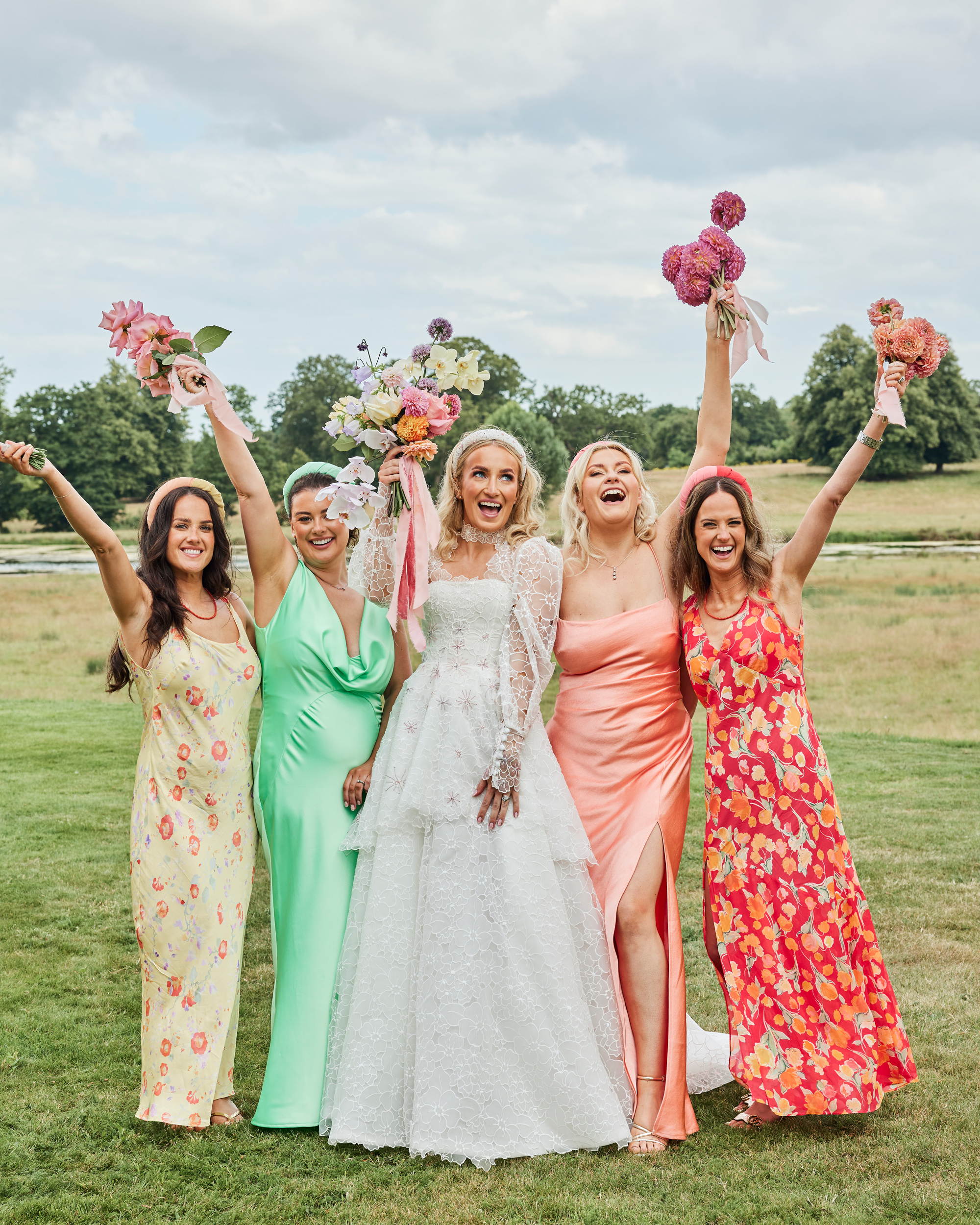 Alex in Emma Beaumont for her Ibiza & Disco Inspired Wedding at Wilderness Reserve 91 Bride with her bridesmaids celebrating in the sunshine, holding vibrant bouquets aloft — a joyful group portrait full of colour, personality and fun, with the bride in a romantic long-sleeved gown.