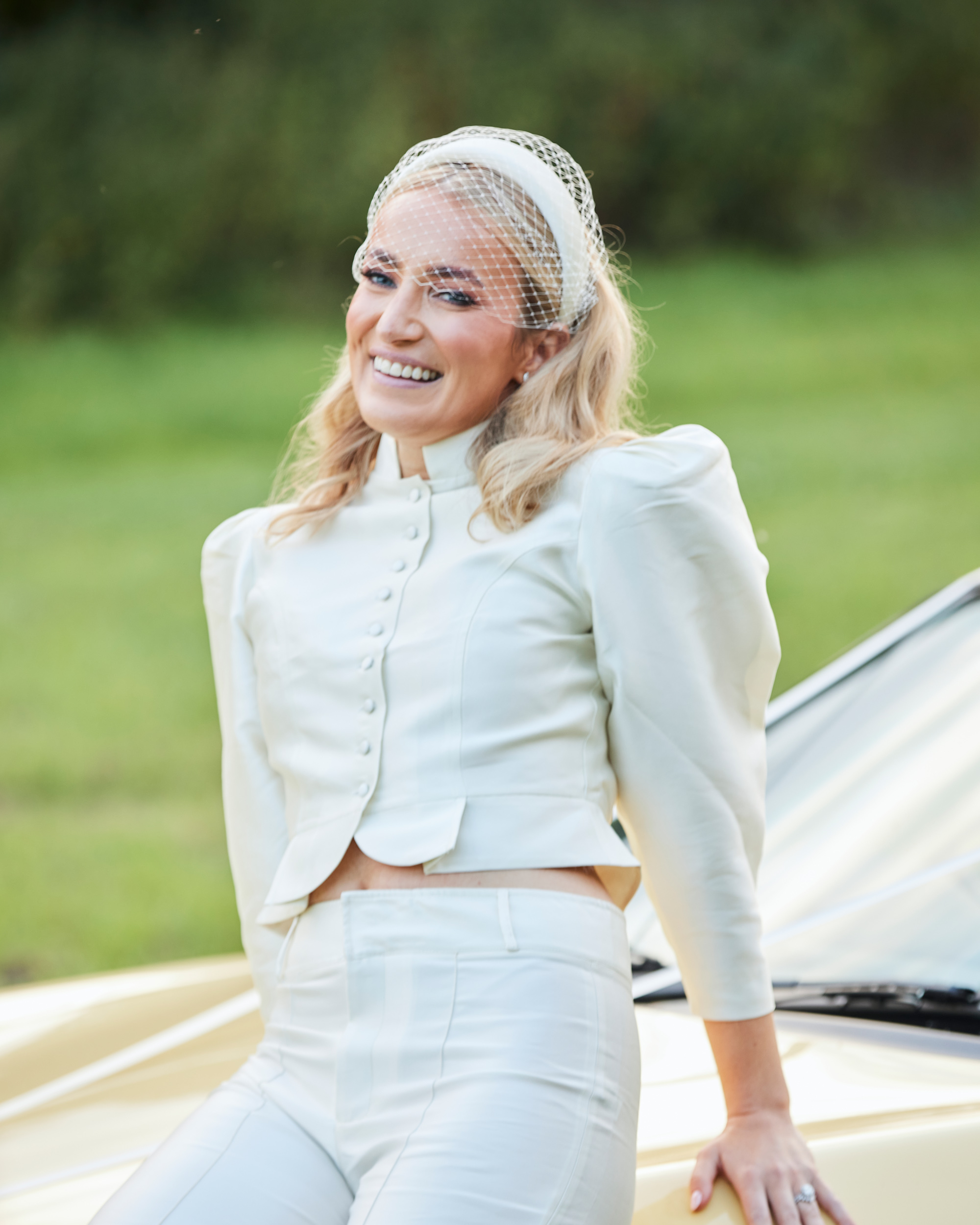 Alex in Emma Beaumont for her Ibiza & Disco Inspired Wedding at Wilderness Reserve 82 Modern bride wearing an ivory satin bridal jumpsuit with structured shoulders and covered buttons, styled with a vintage-inspired headband veil — effortlessly cool wedding day fashion.