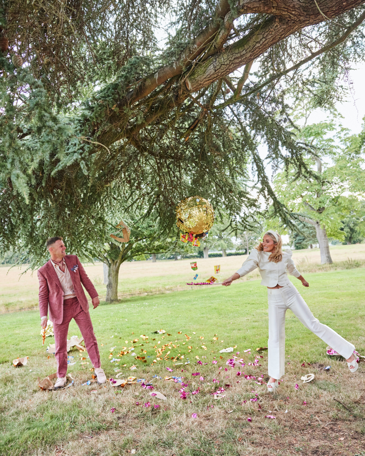 Alex in Emma Beaumont for her Ibiza & Disco Inspired Wedding at Wilderness Reserve 90 Bride and groom enjoy a fun moment outdoors smashing a gold piñata, with colourful confetti and sweets flying — a vibrant and unexpected wedding day celebration full of personality and laughter.