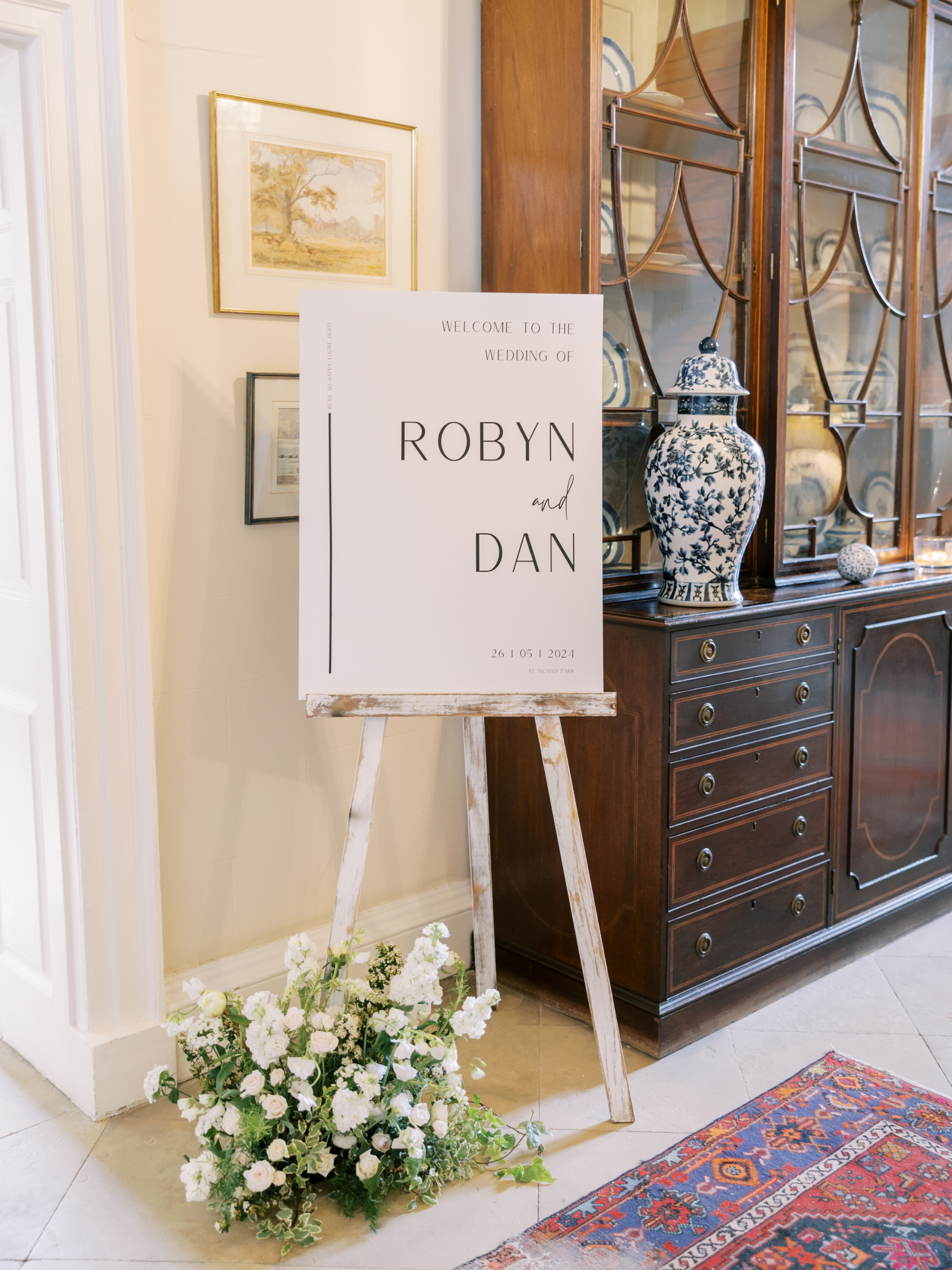 Elegant wedding signpost on a white easel with flowers by the base.