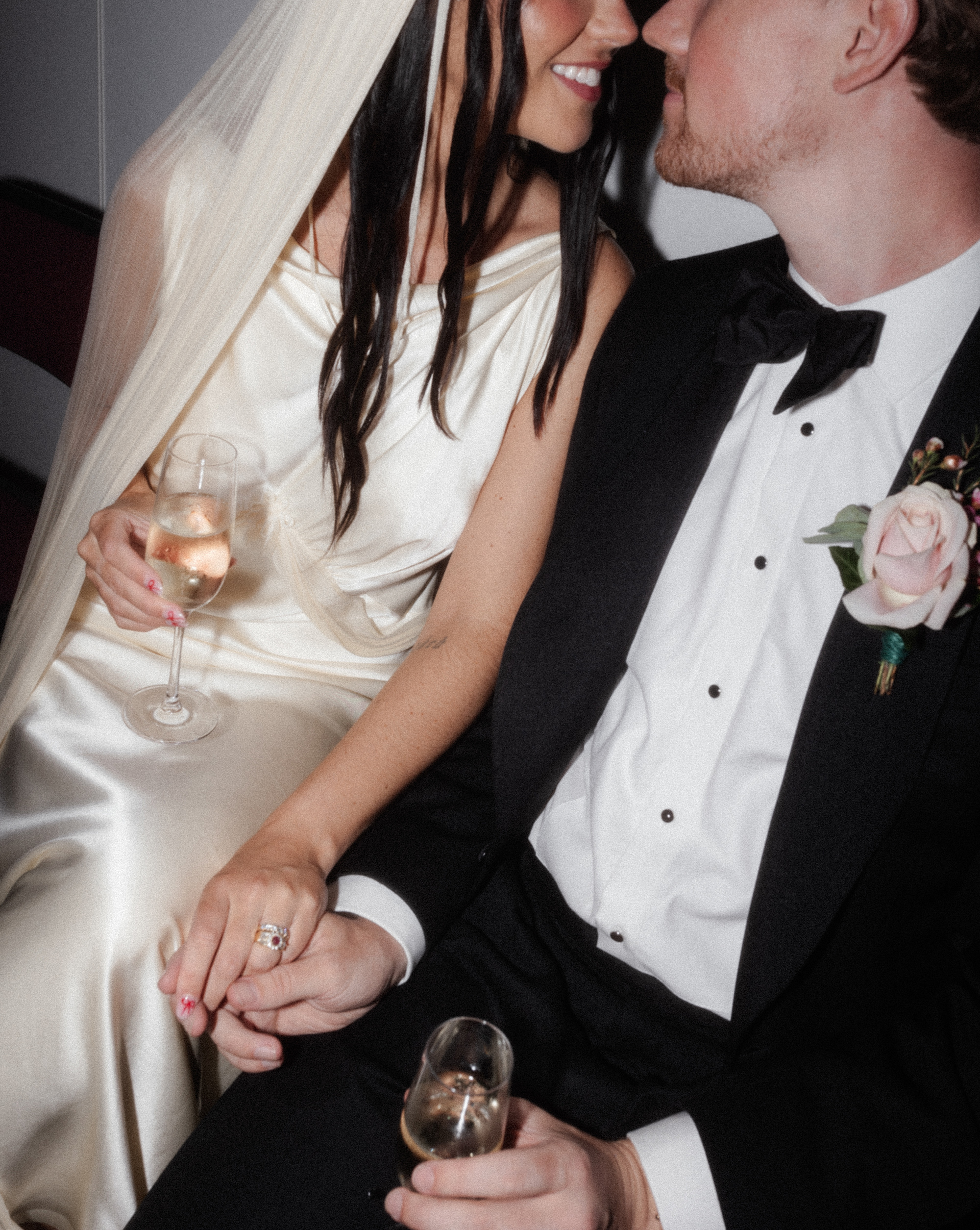 Close up shot of bride and groom cosying up to one another with glasses of champagne.