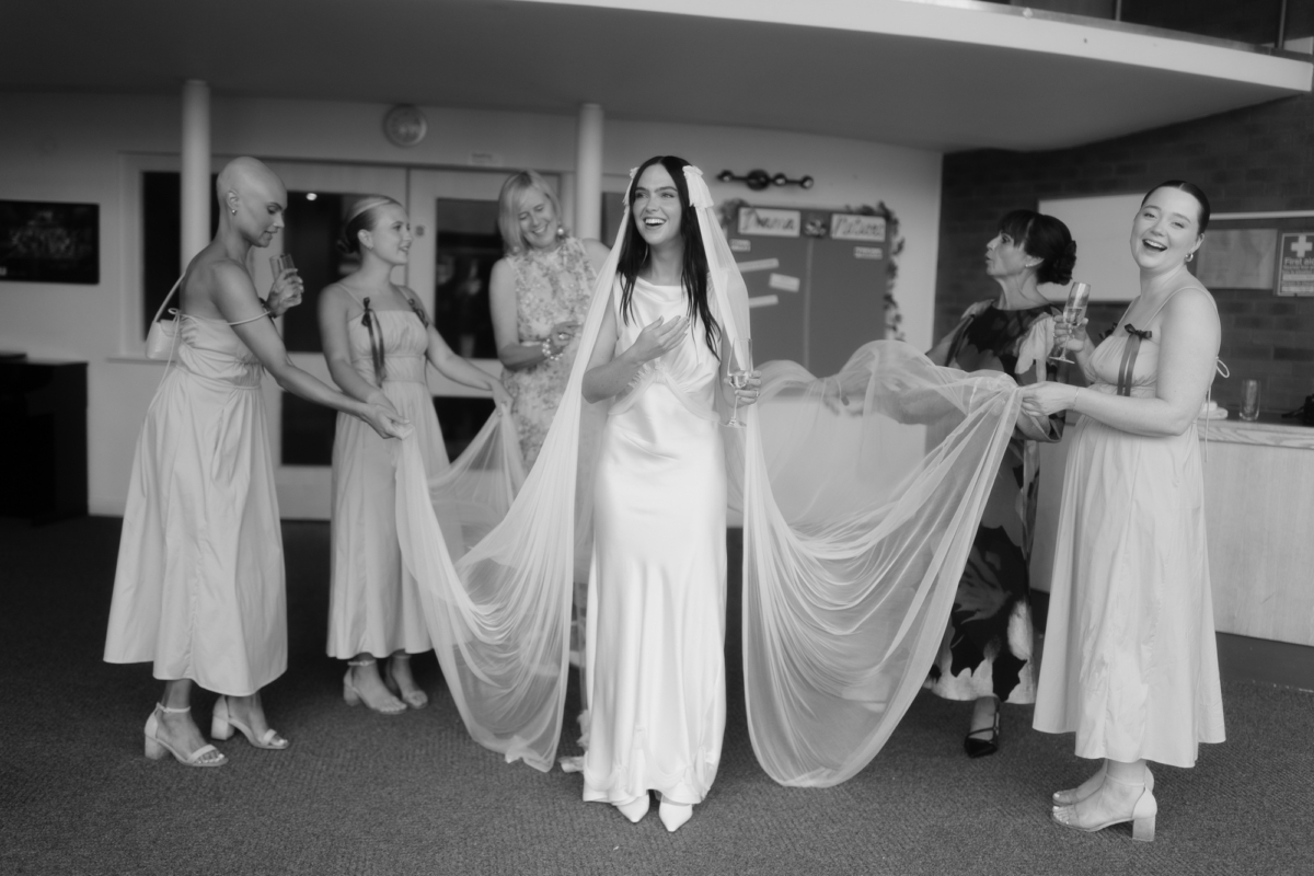 Bride wearing a Paula Nanda wedding dress and veil with fringe/tassel details - her bridesmaids carrying the edge of her veil.