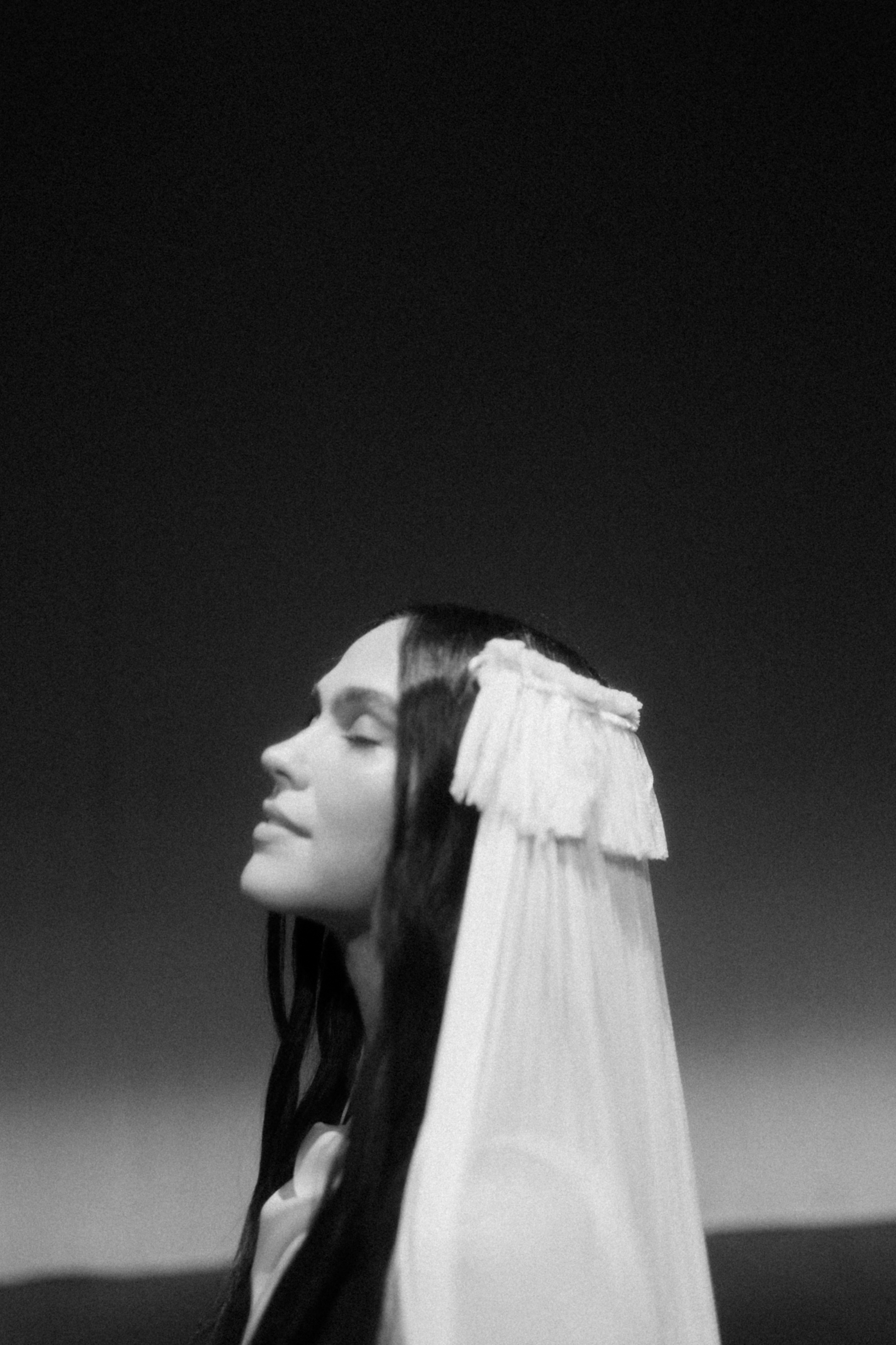 Artistic photograph of a bride's facial profile as she closes her eys gently. She has long dark hair and wears a fringed wedding veil.