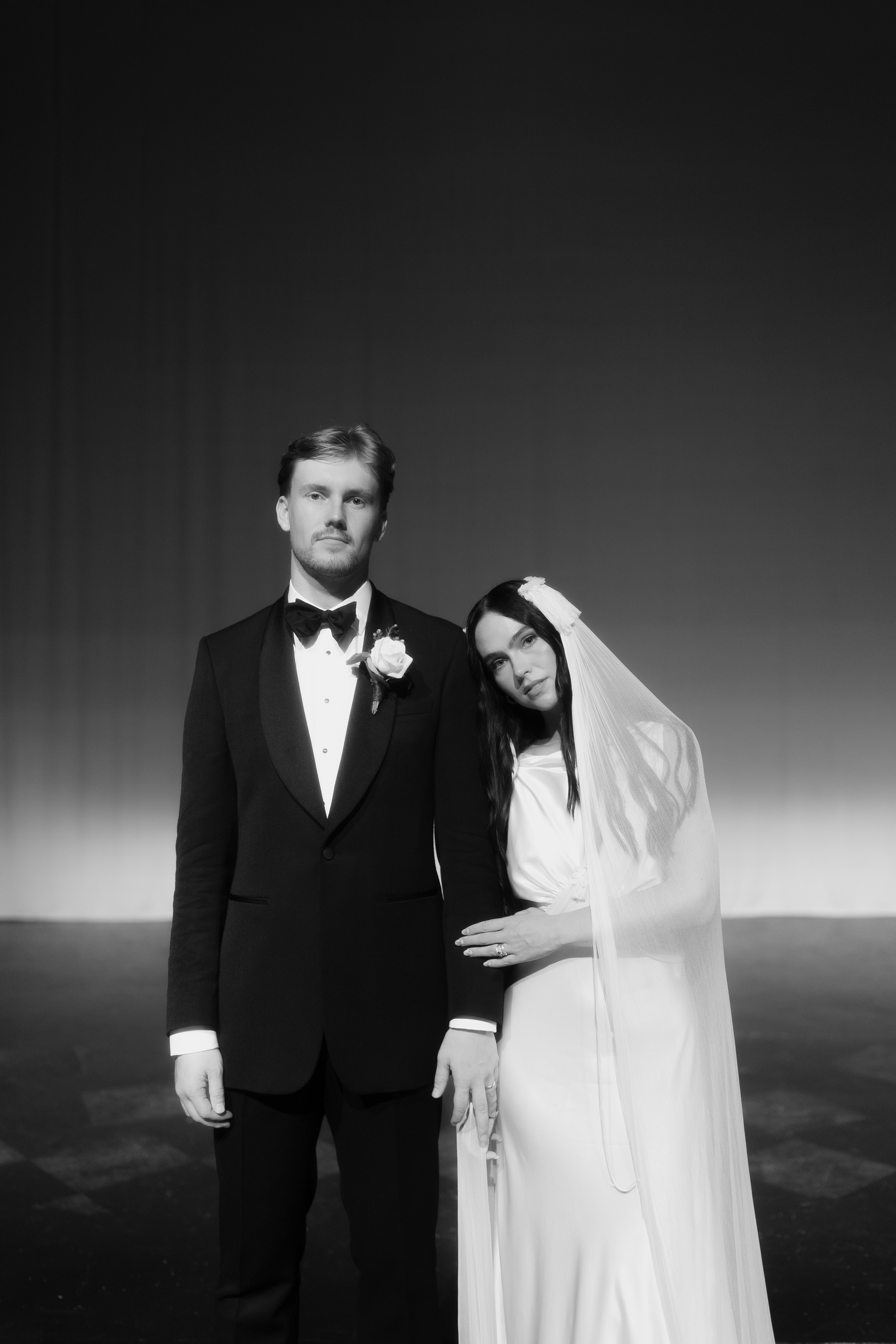 Black and white wedding photography, groom in black tie and bride in a fringed and tasseled veil and dress by Paula Nanda.