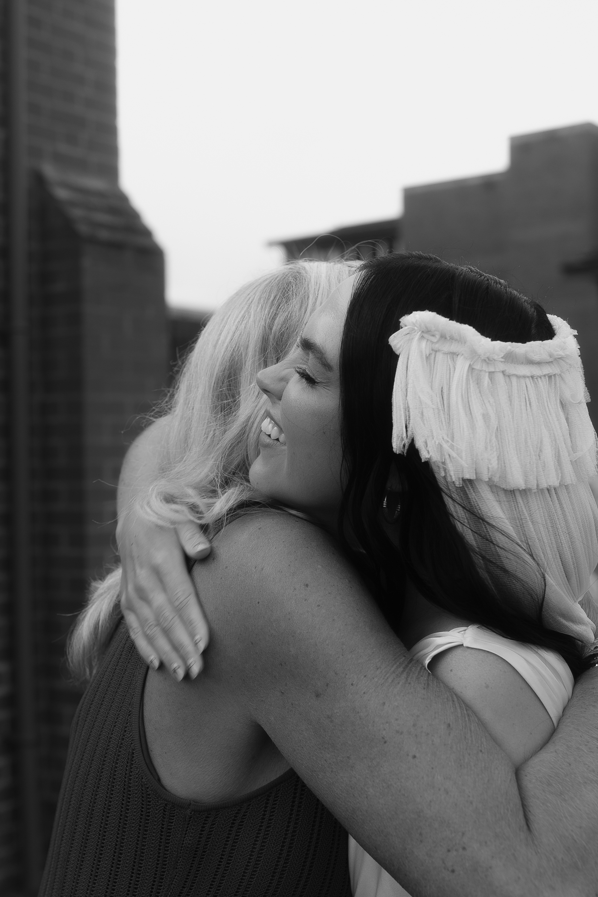 Bride with a fringed tasseled wedding veil by Paula Nanda - hugging a wedding guest.