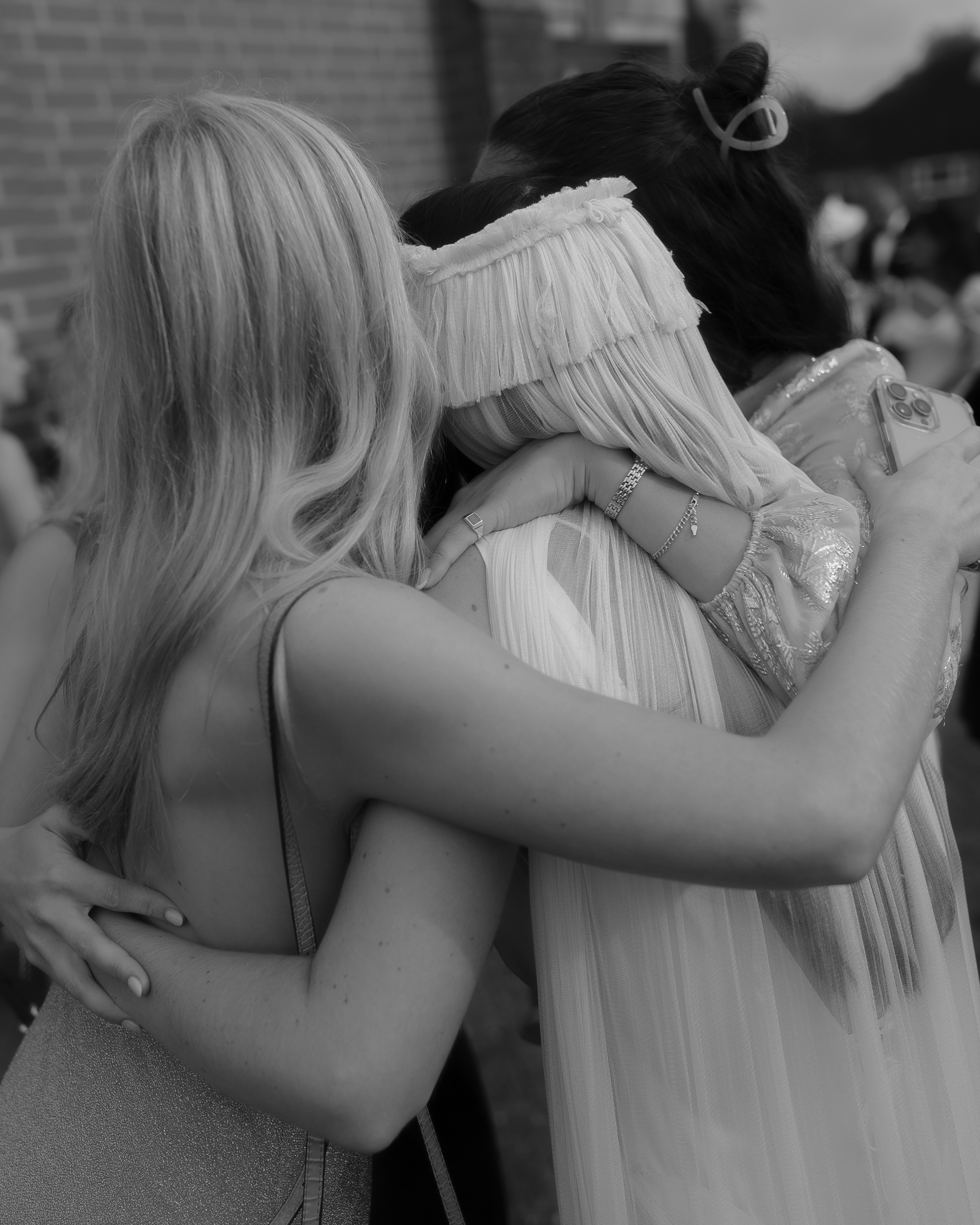 Back shot of a bride with a fringed wedding veil bing hugged by her guests.