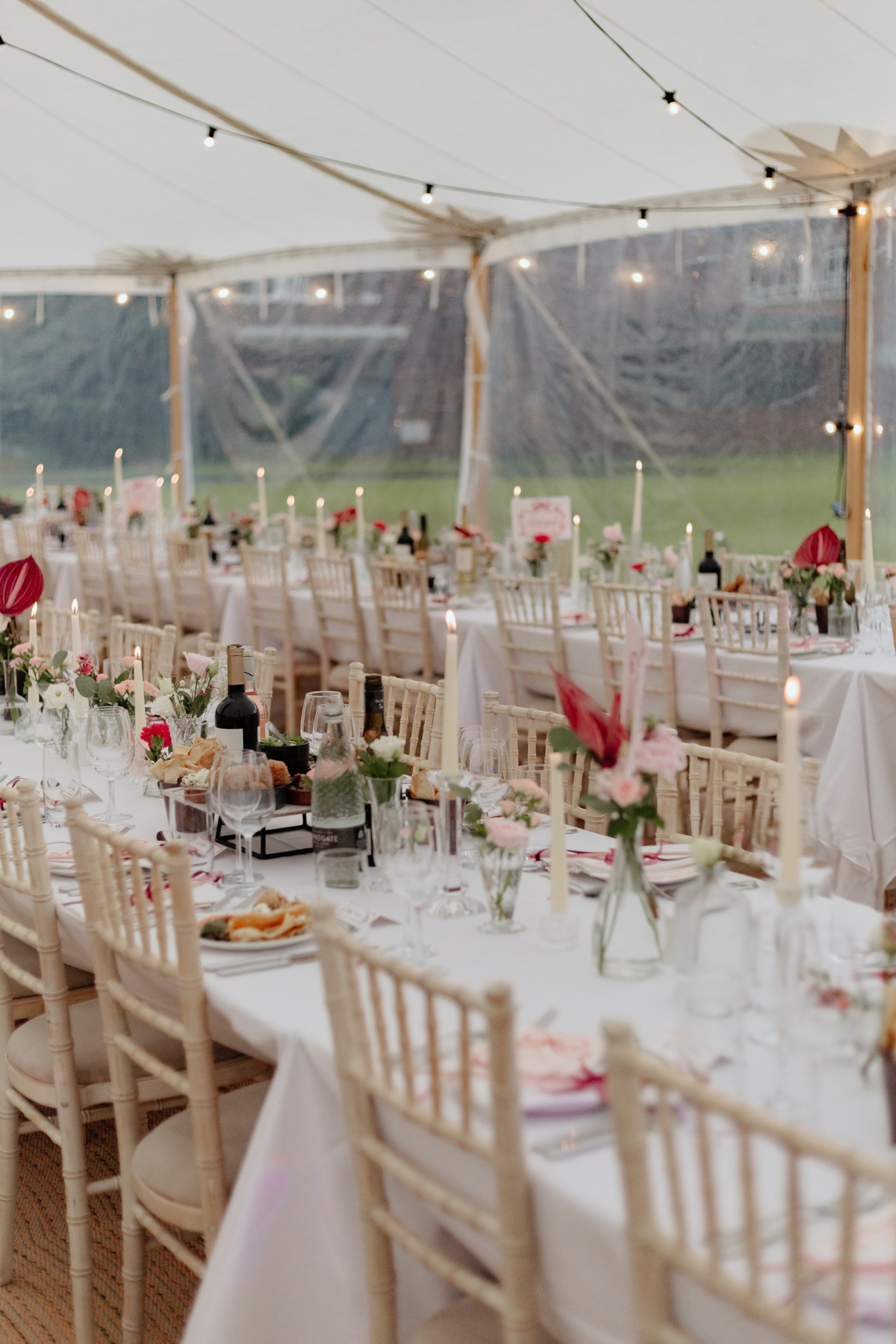 Inside a wedding marquee with white taper candles, festoon lights, pink flowers and pink accents.