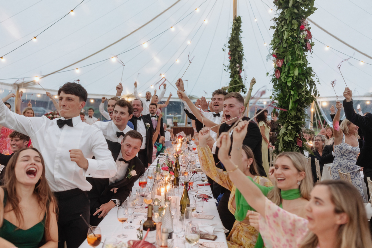 Wedding guests standing and waving wooden sticks with fabric on the end to welcome the bride and groom.