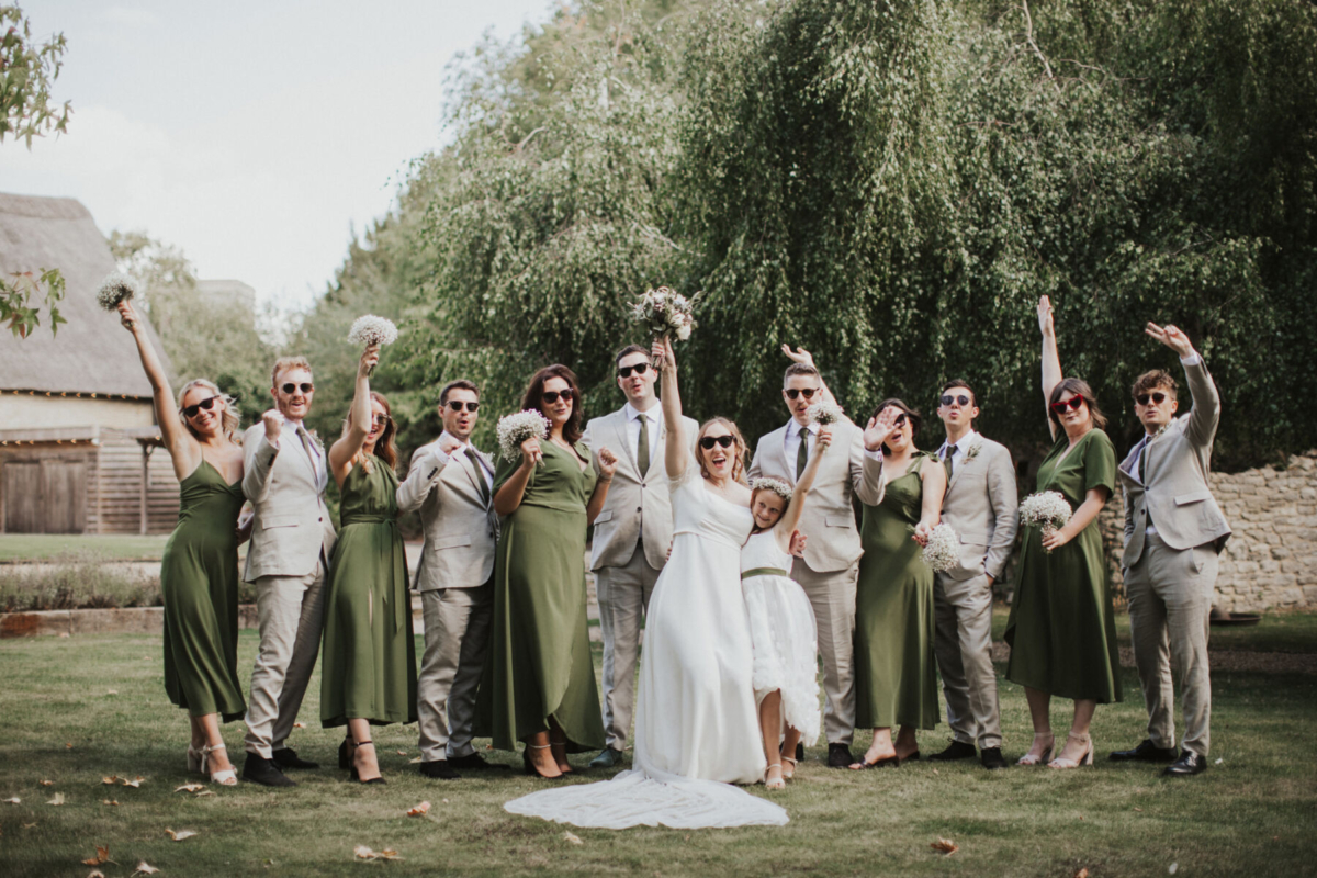 How A Bridal Fashion Stylist Planned Her Wedding at Tythe 15 Tythe Barn wedding in Oxfordshire. Bride and groom lined up with the bridesmaids in green dresses.