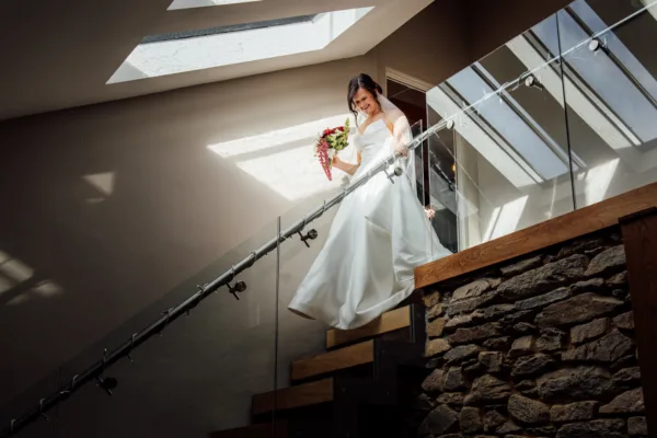A bride walks down stairs in natural light during her wedding at Trevenna in Cornwall.