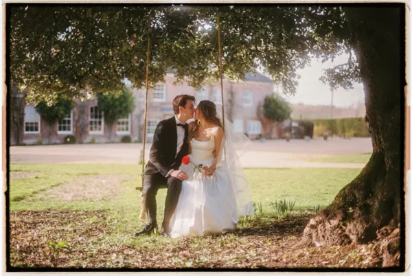 A bride and groom embrace whilst sat on a swing at their wedding.