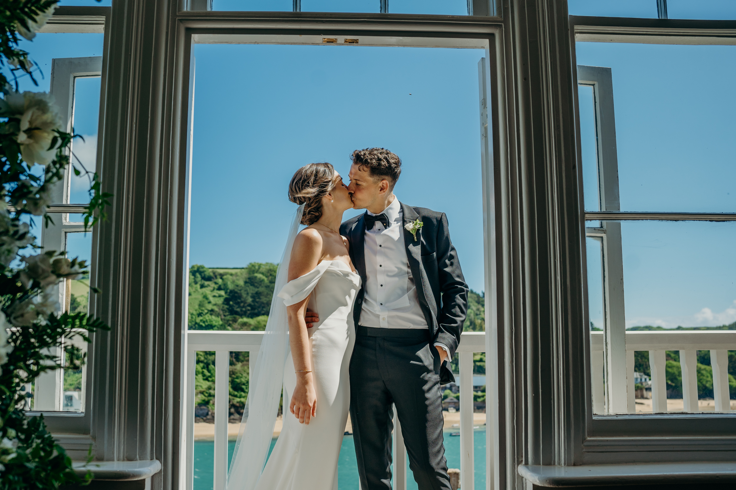 Bride and groom kissing at their Salcombe Devon Wedding the sea in the distance behind them.