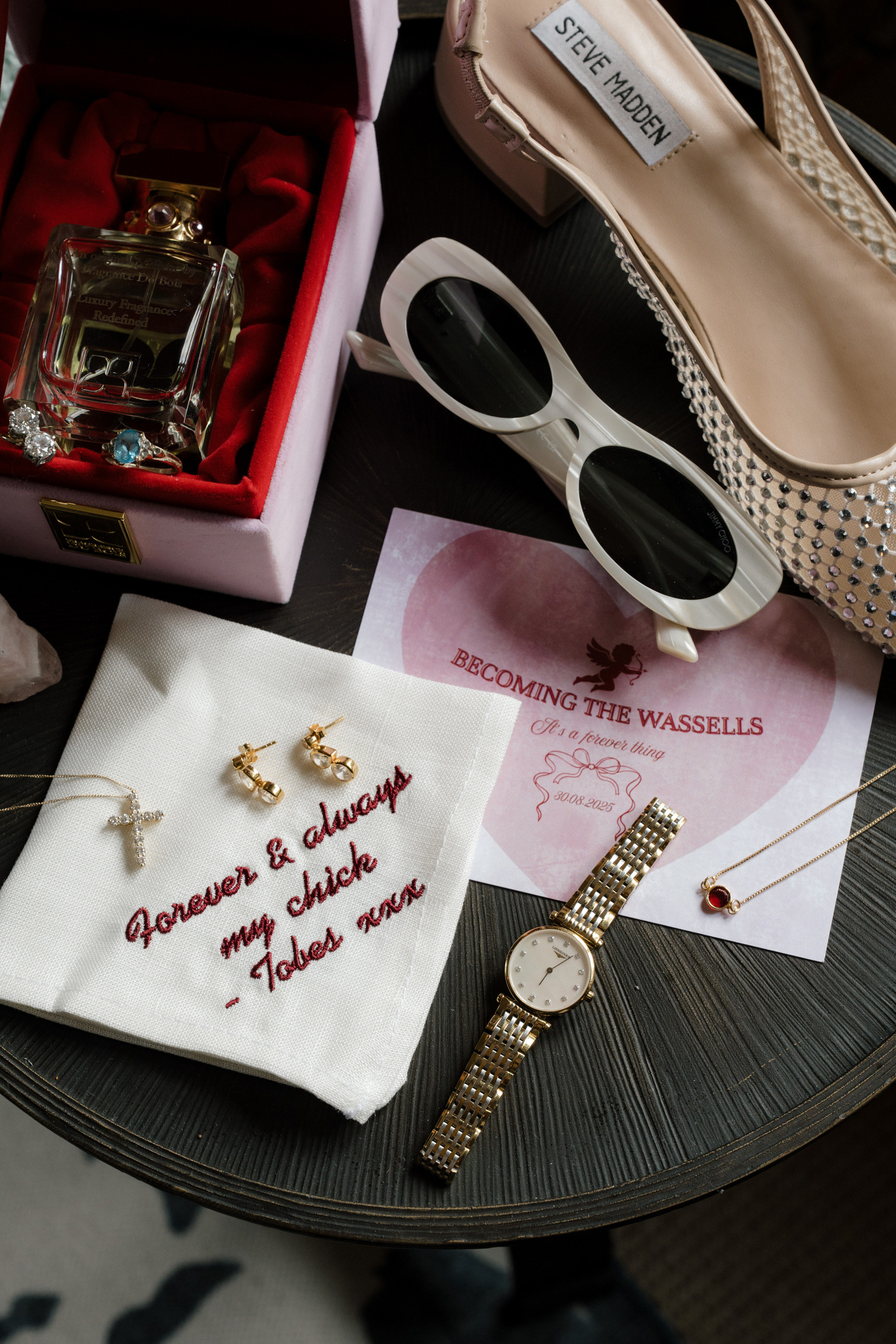 Flat lay of bridal accessories including a handkerchief with embroidery, sunglasses, and Steve Madden shoes.
