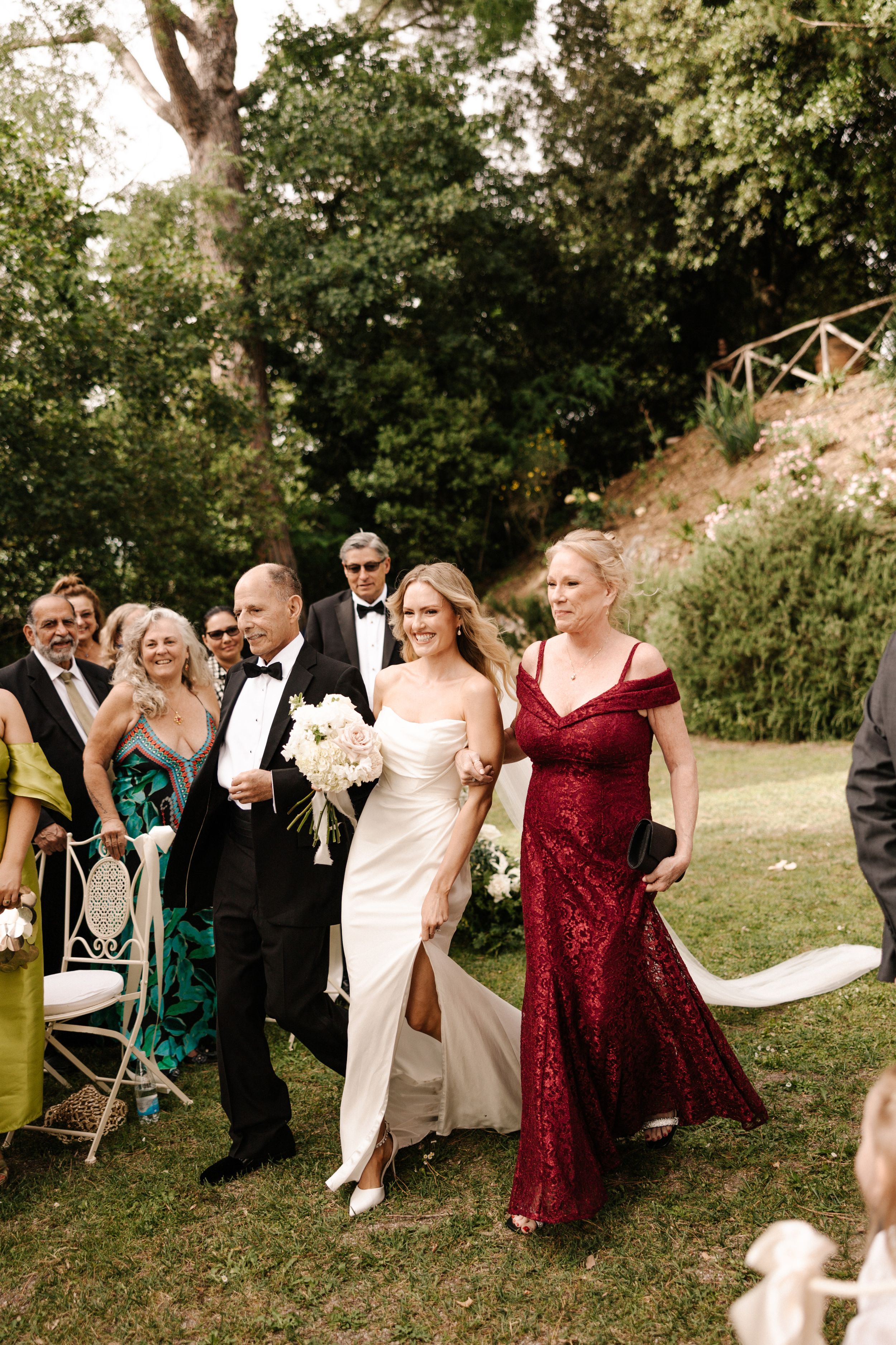 image - A Modern, Romantic Destination Wedding at Borgo Sant Ambrogio in Tuscany Bride walking arm in arm with her mother and father into her wedding ceremony in the gardens of Borgo Sant Ambrogio in Tuscany, Italy.