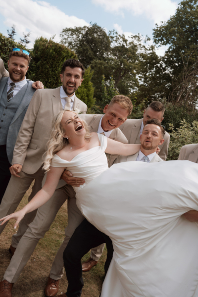 Fun photo of bride being picked up by groom and groomsmen